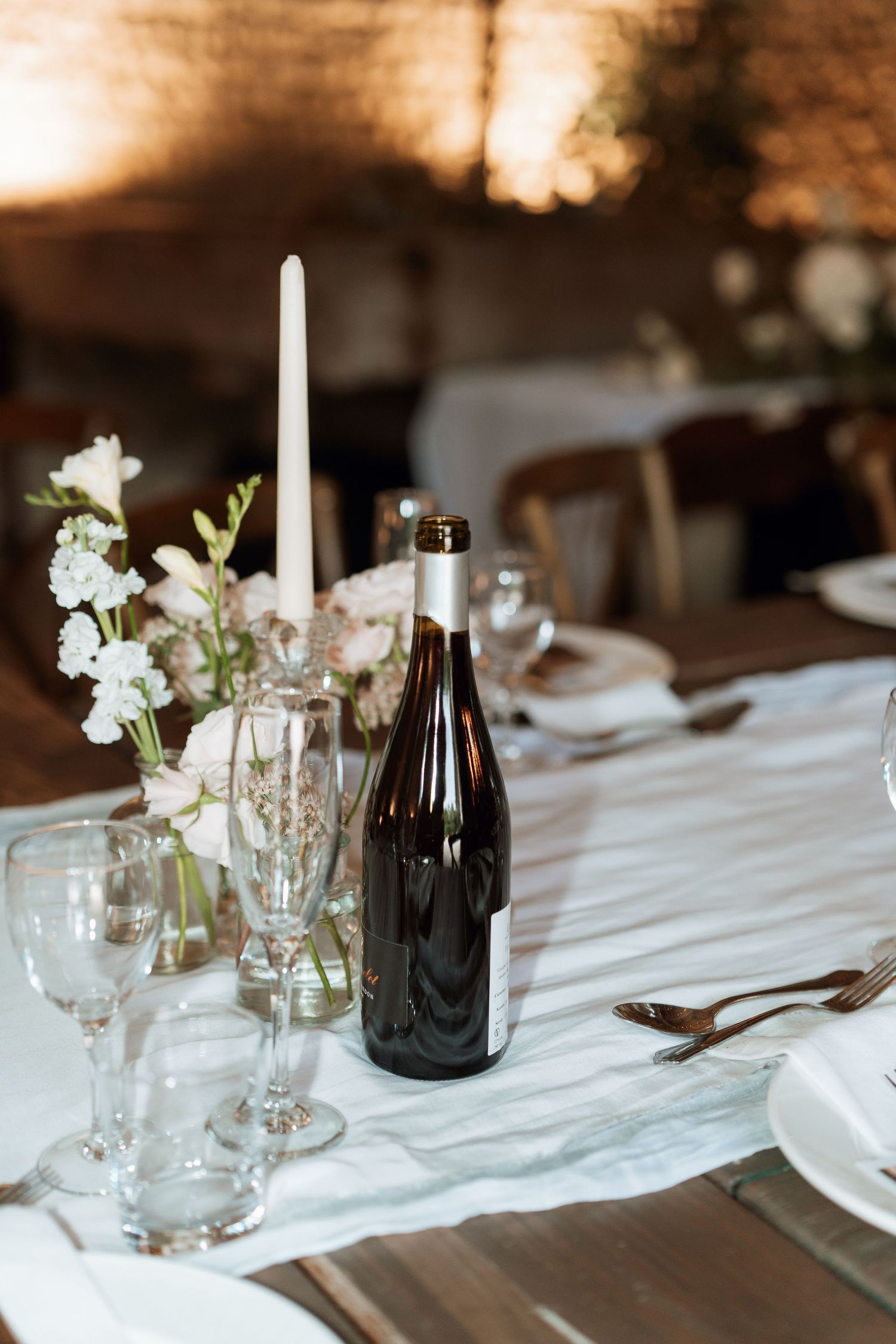 Elegant wedding table settings with white linens, candles, and delicate floral arrangements in a rustic venue.