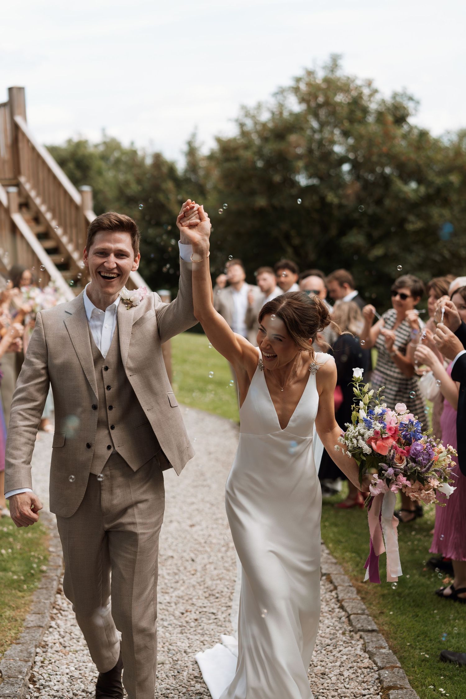 Newlyweds celebrating while walking down a gravel path as guests cheer.