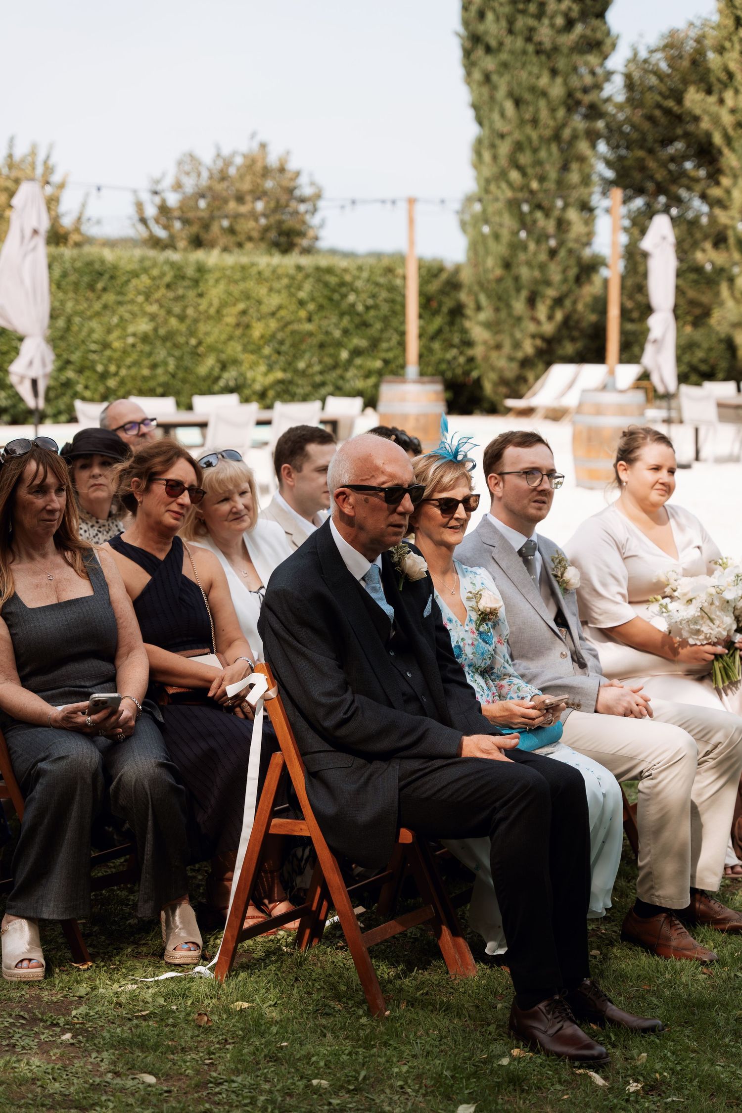 Guests seated in wooden chairs at an outdoor ceremony.