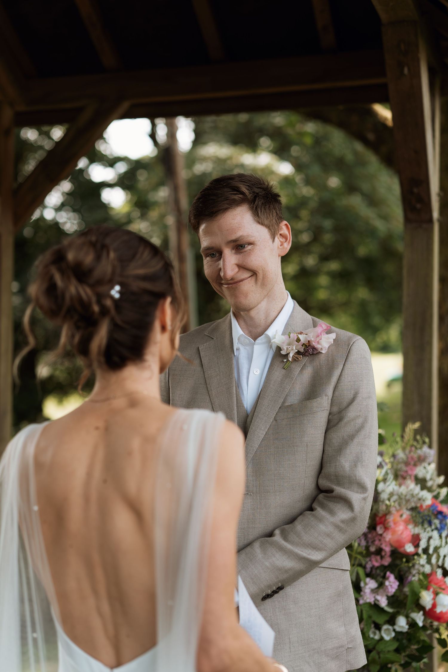 Intimate wedding ceremony moment under wooden gazebo with colorful floral arrangements.