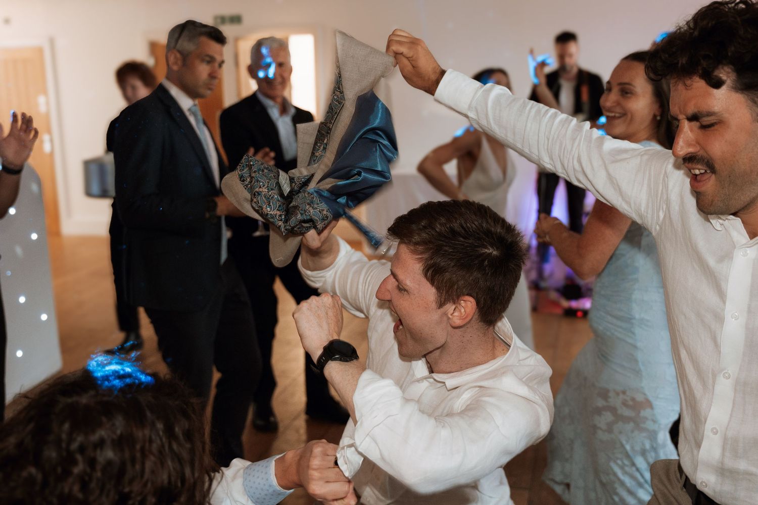 Wedding reception guests dancing and celebrating in an indoor venue with string lights.