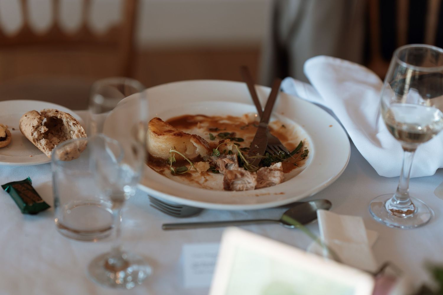 An elegant plated dinner setting with wine glasses and a gourmet meal on white tablecloth.