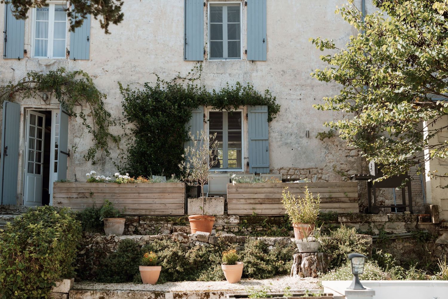Stone exterior of a French country house with blue shutters and potted plants.