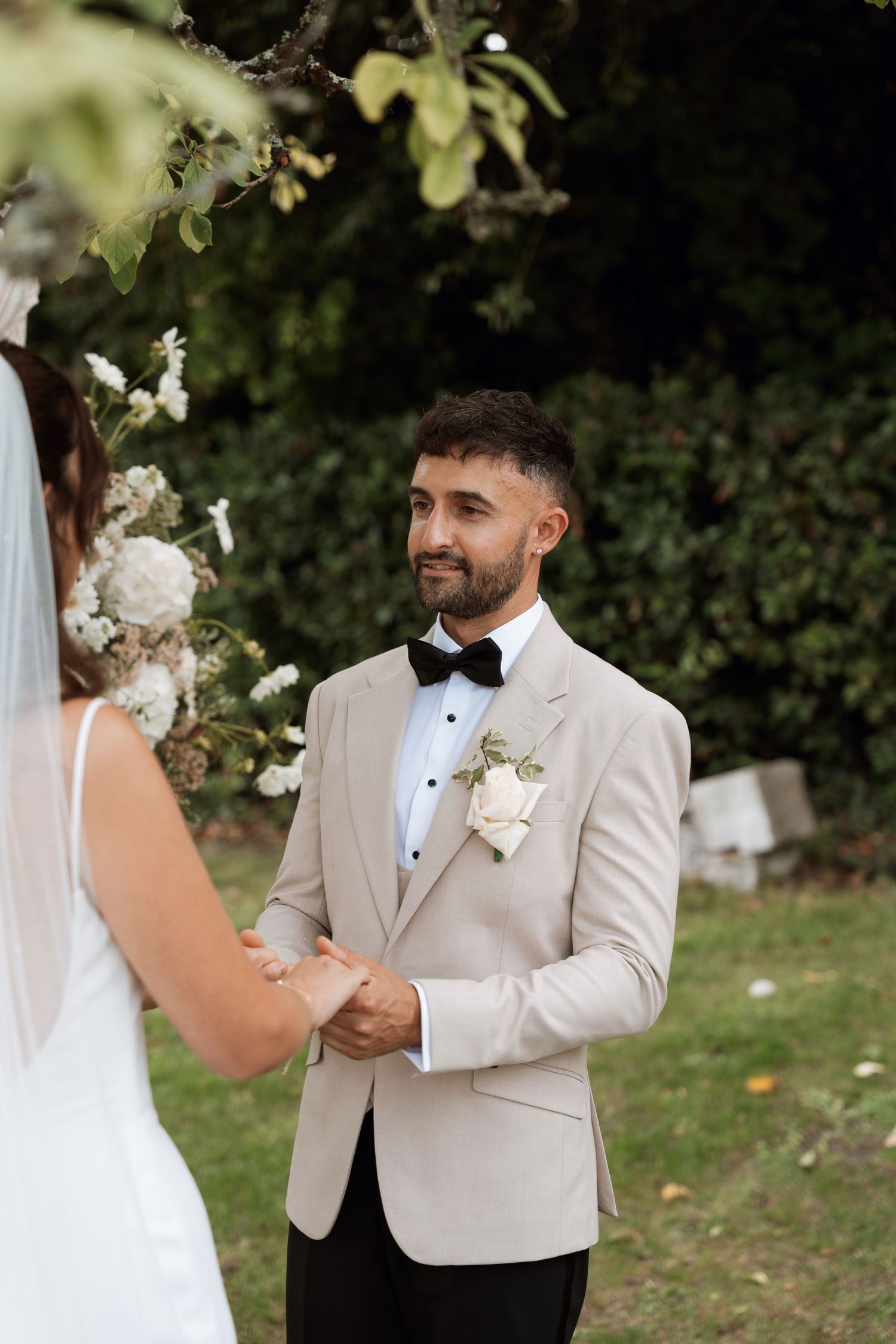 Wedding ceremony moment captured outdoors with white floral decorations and greenery.