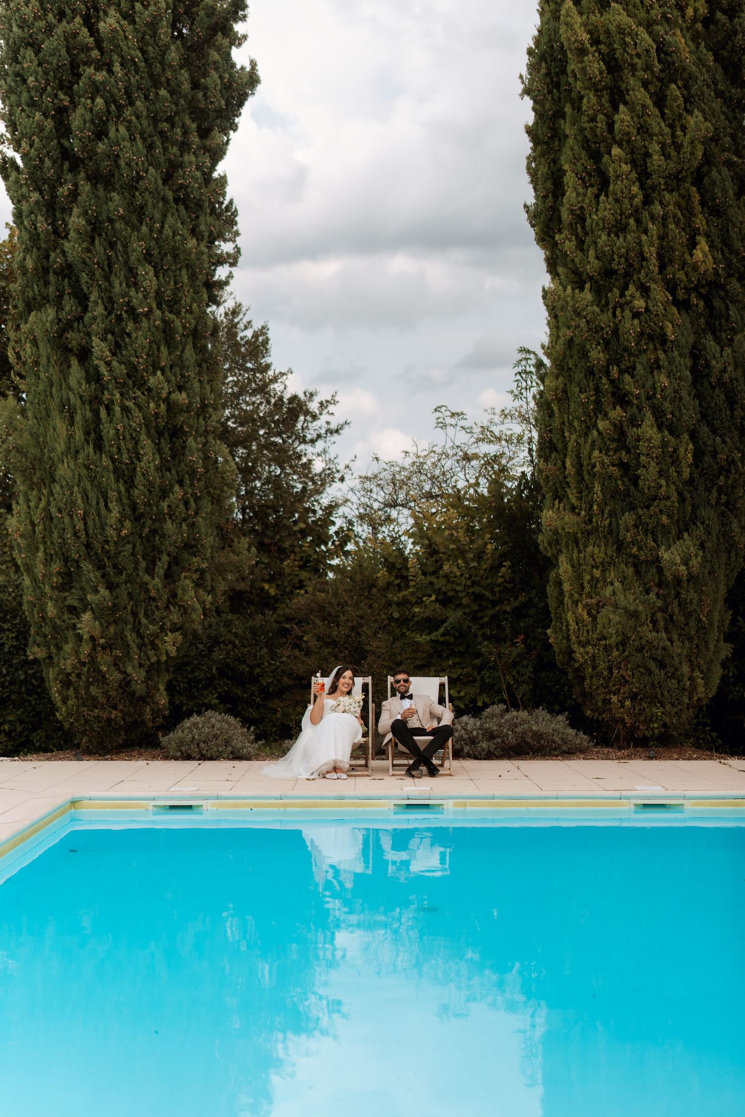 Bright turquoise swimming pool surrounded by tall cypress trees in a French countryside setting.