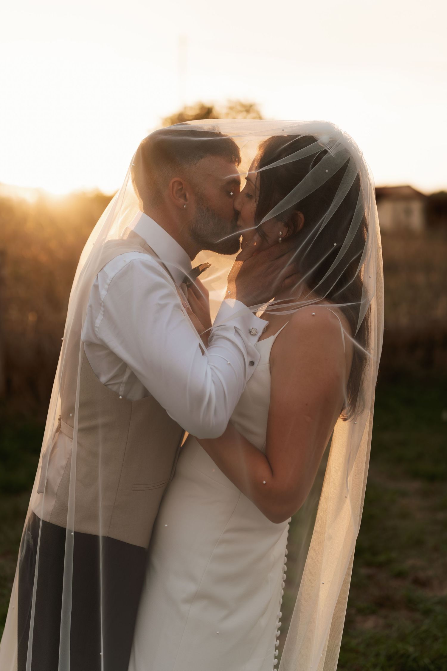 Intimate wedding couple portrait at sunset with flowing white veil.