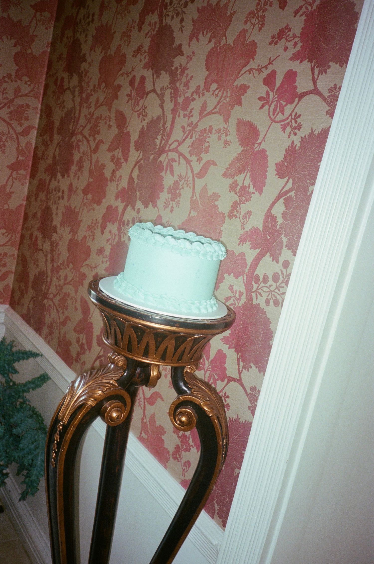 A decorative wall with pink floral wallpaper and white trim features an ornate gold-framed mirror or stand.
