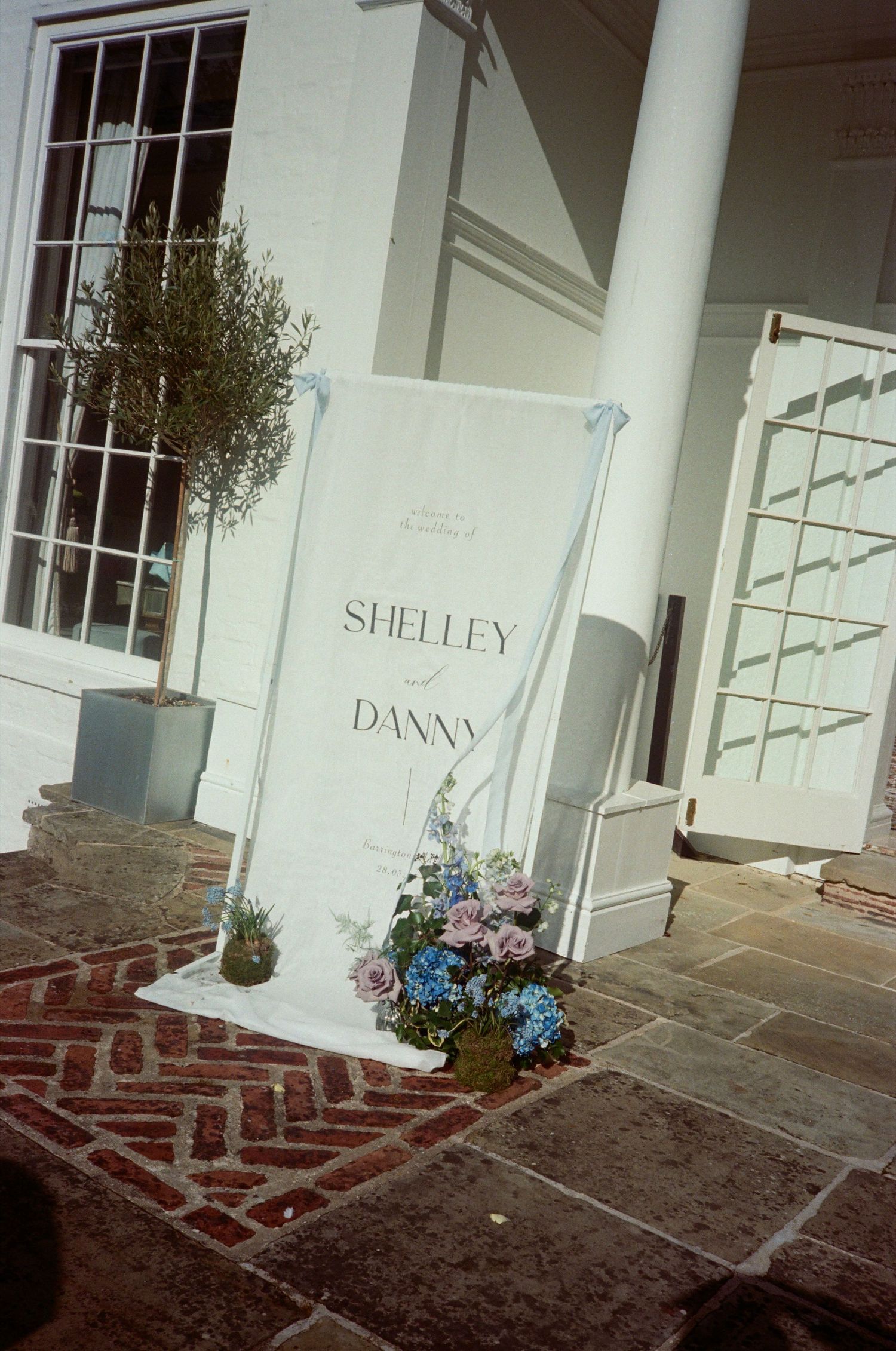 A series of connected images showing a white building entrance with names on the wall and flowers in planters.