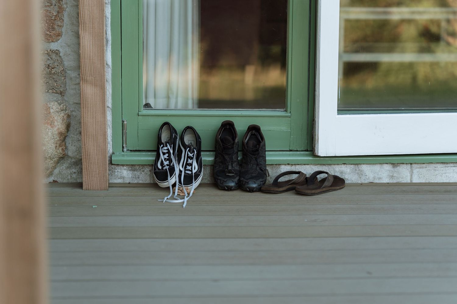 A collection of black shoes and sandals lined up on a windowsill with green trim.