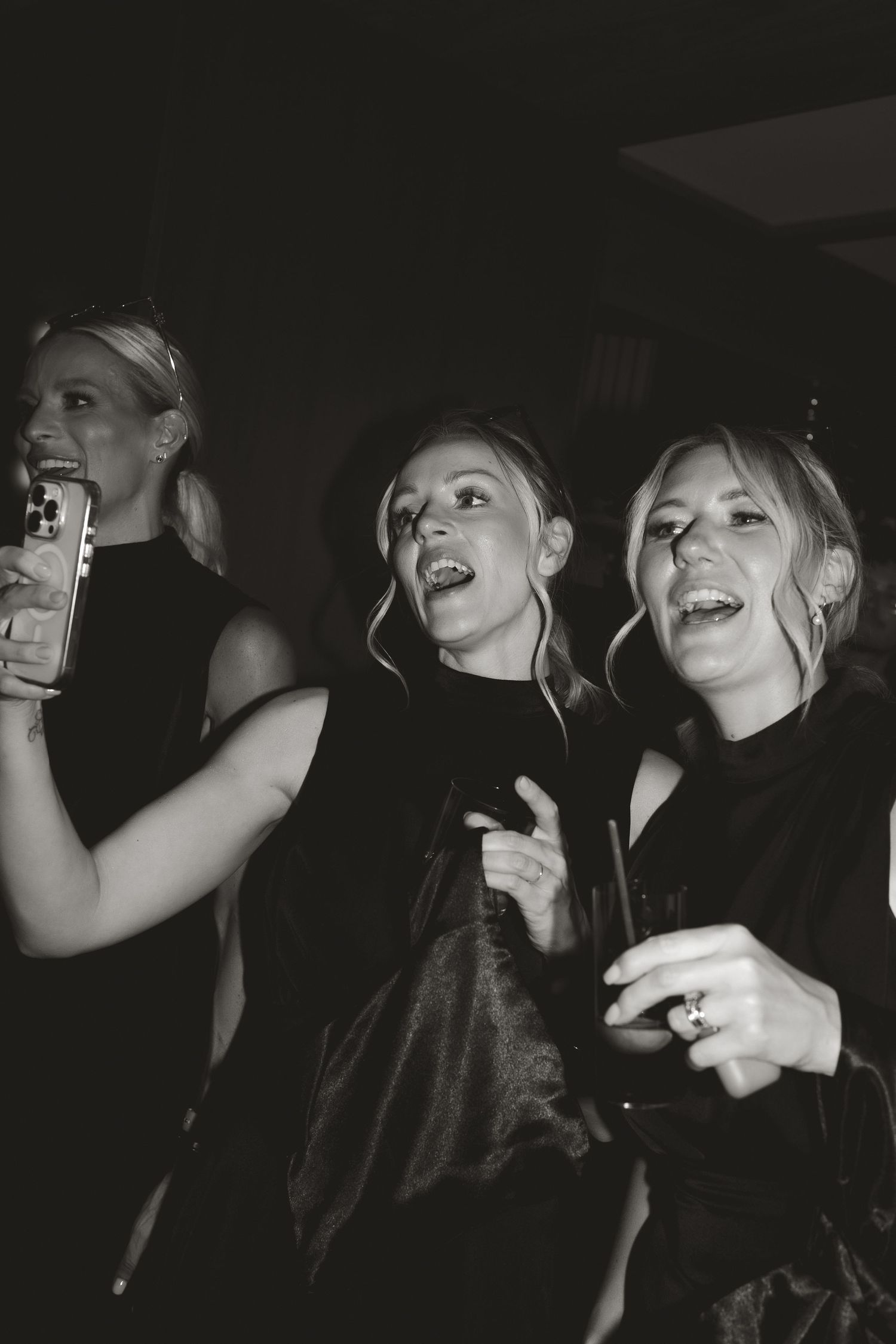 Black and white photo of party-goers dancing and laughing in a dark nightclub setting.