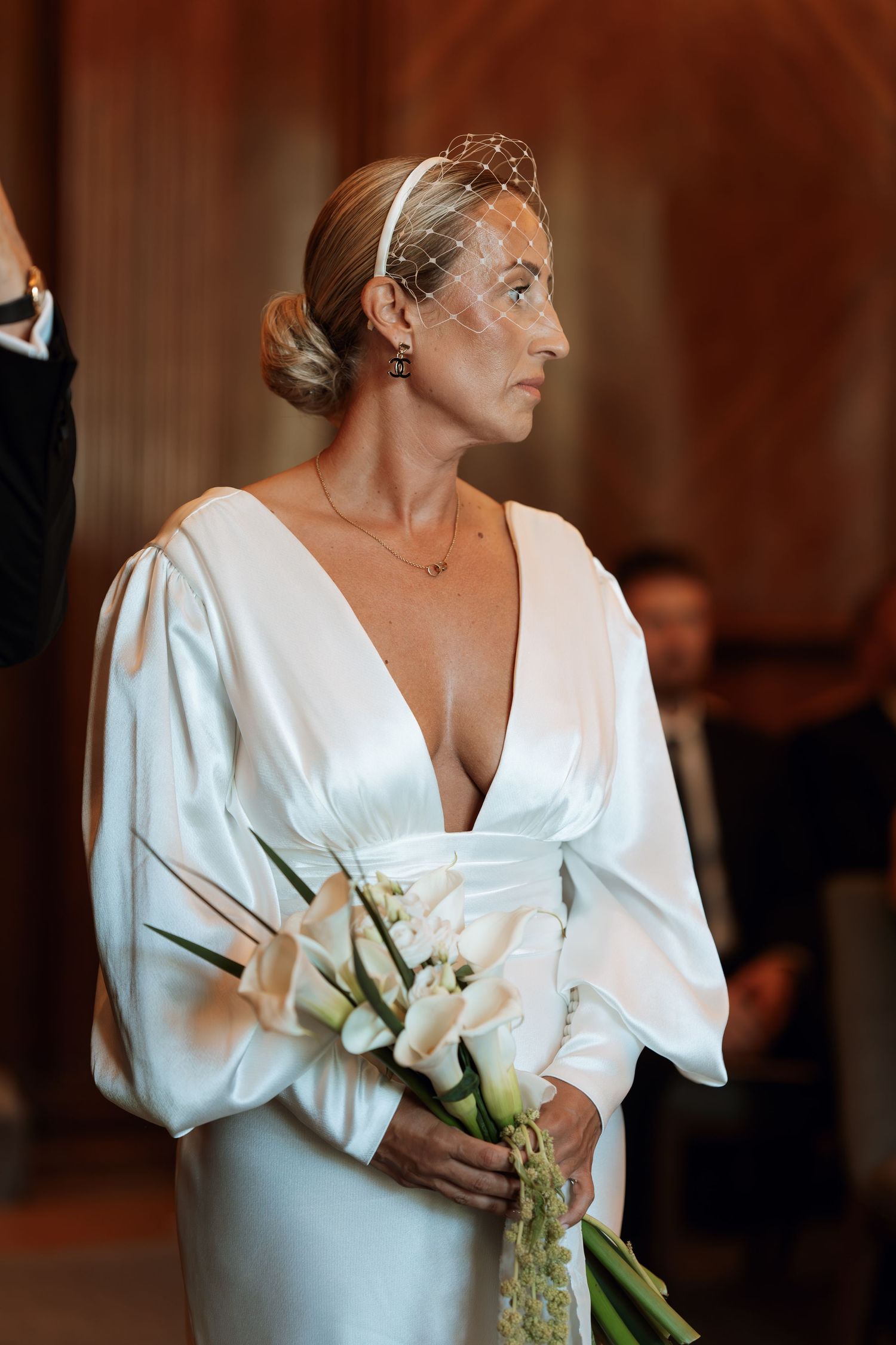 Bride in elegant white dress holds a delicate bouquet while looking to the side in an intimate moment.