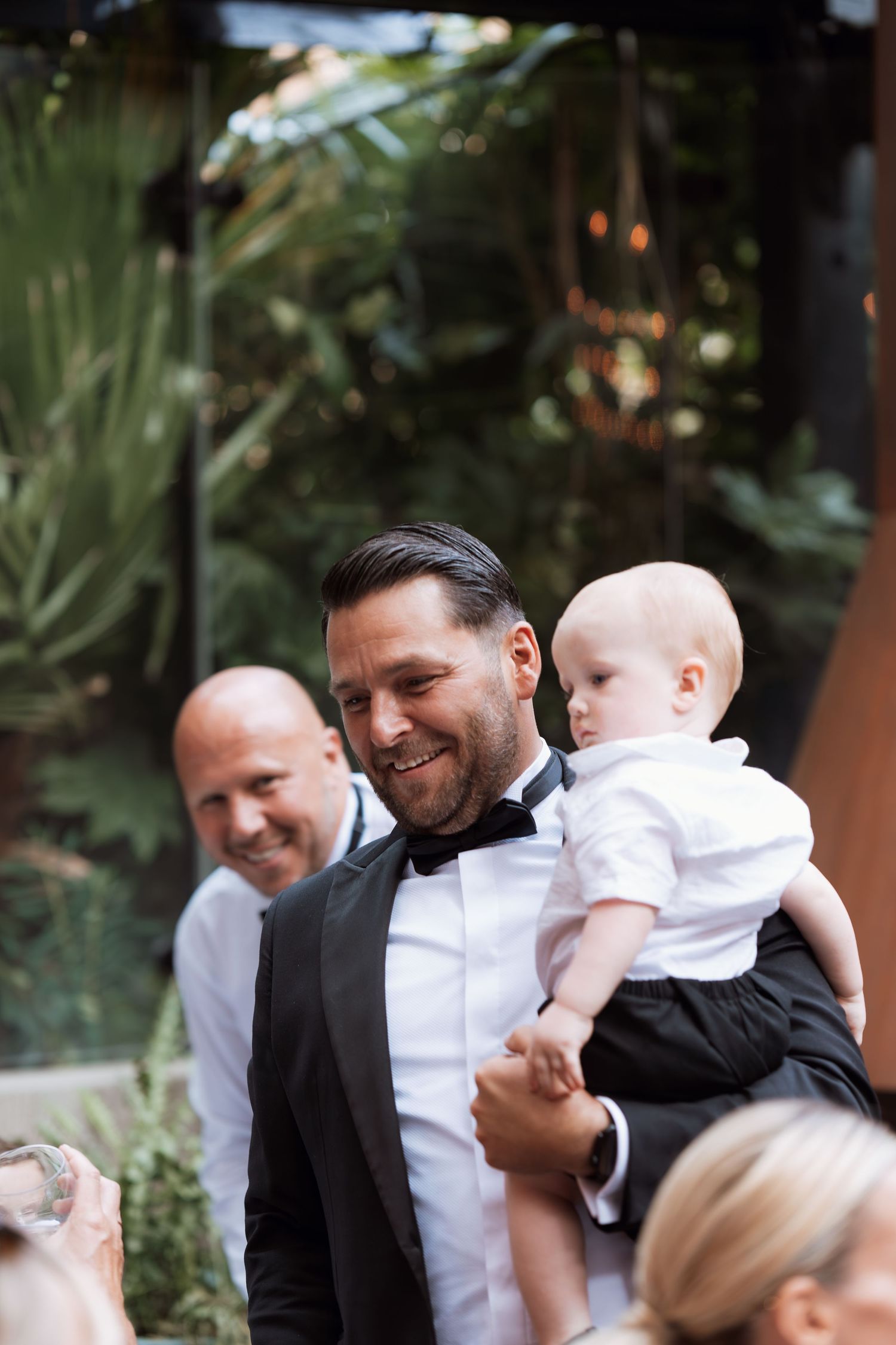 A joyful moment at a garden wedding reception with formal attire and tropical plants.