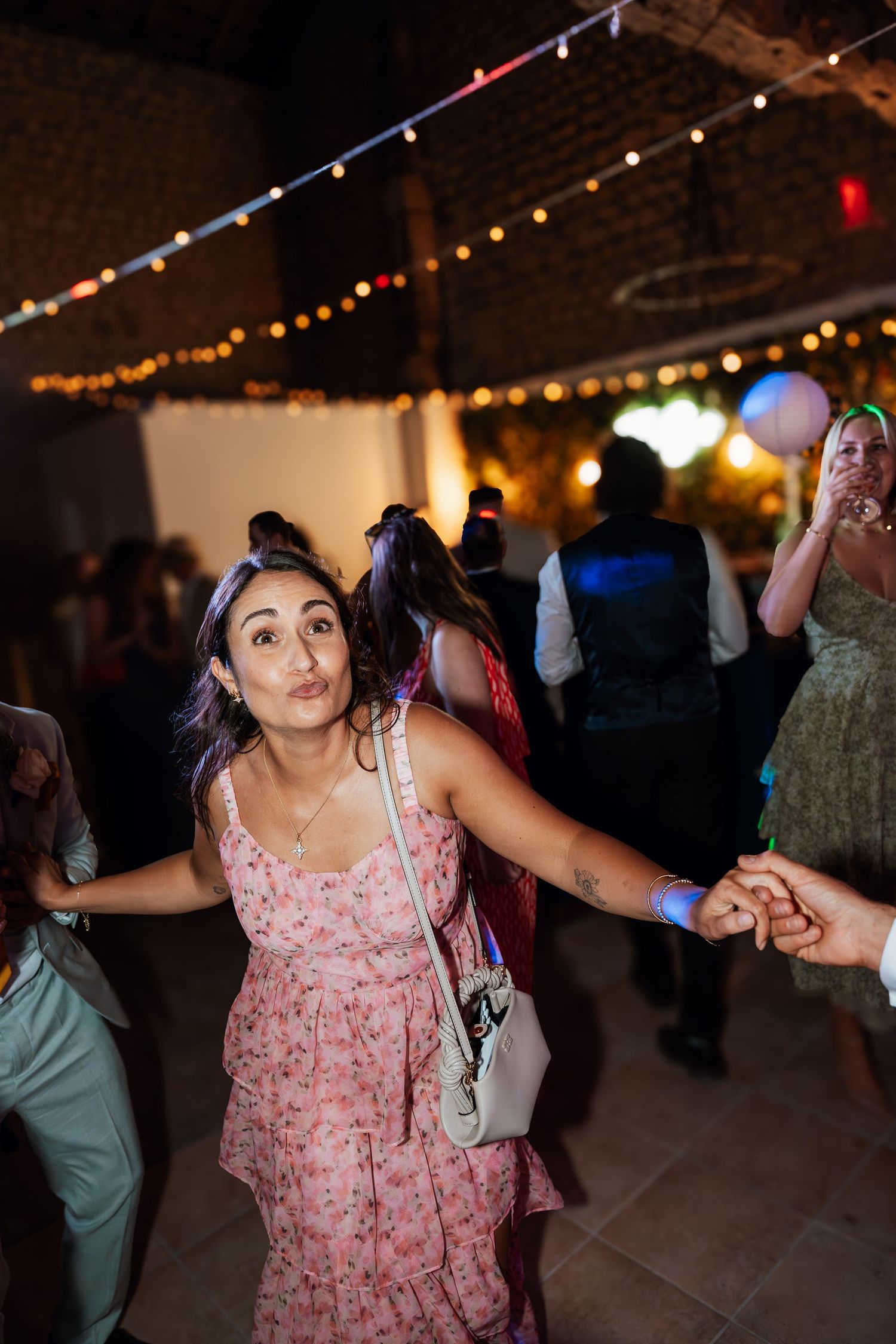 Wedding reception dance floor with string lights overhead and guests dancing in pink dresses.