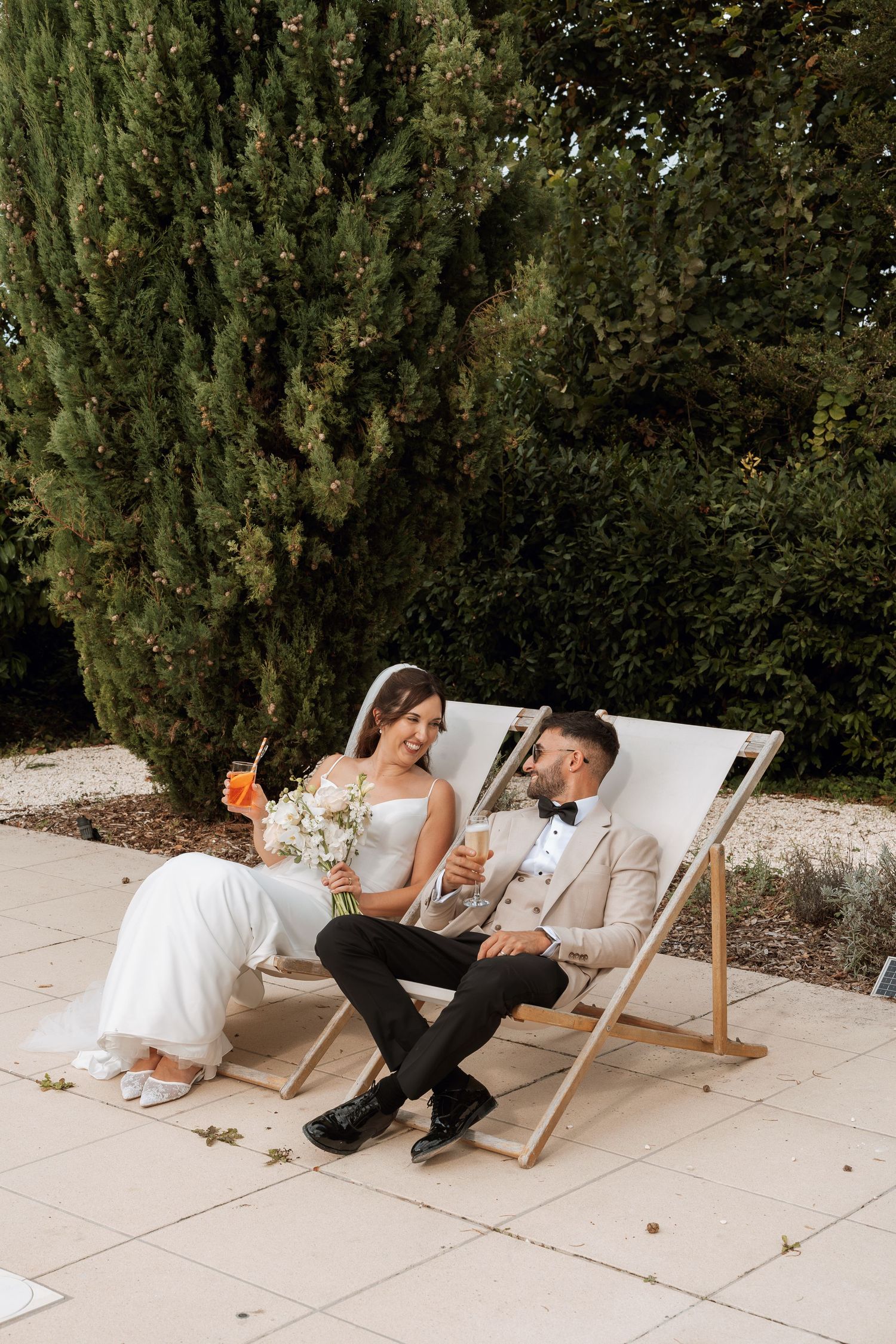 Newlyweds relax together in white deck chairs on a sunny terrace.
