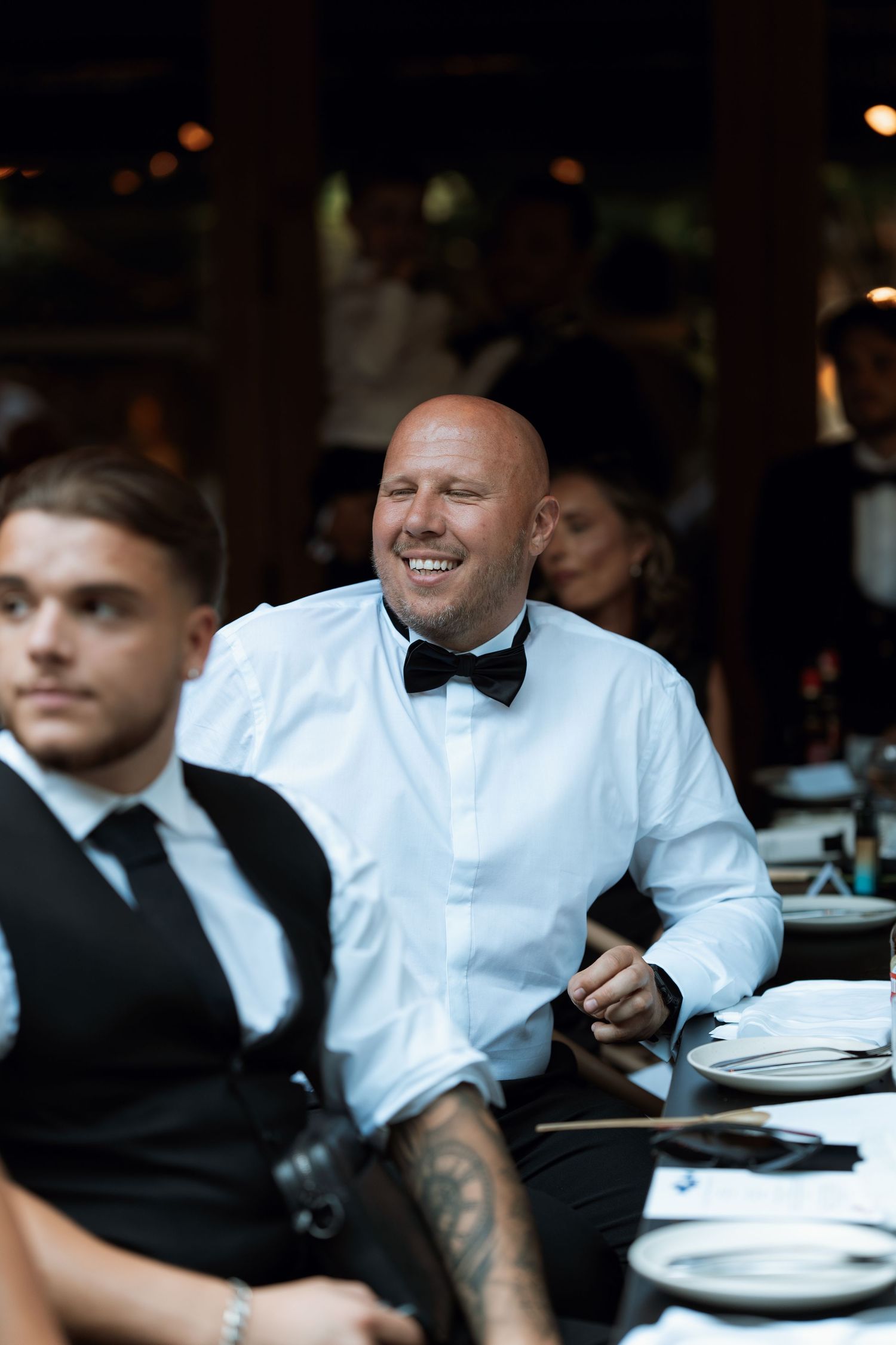Wedding reception guests in formal attire gather around dining tables.