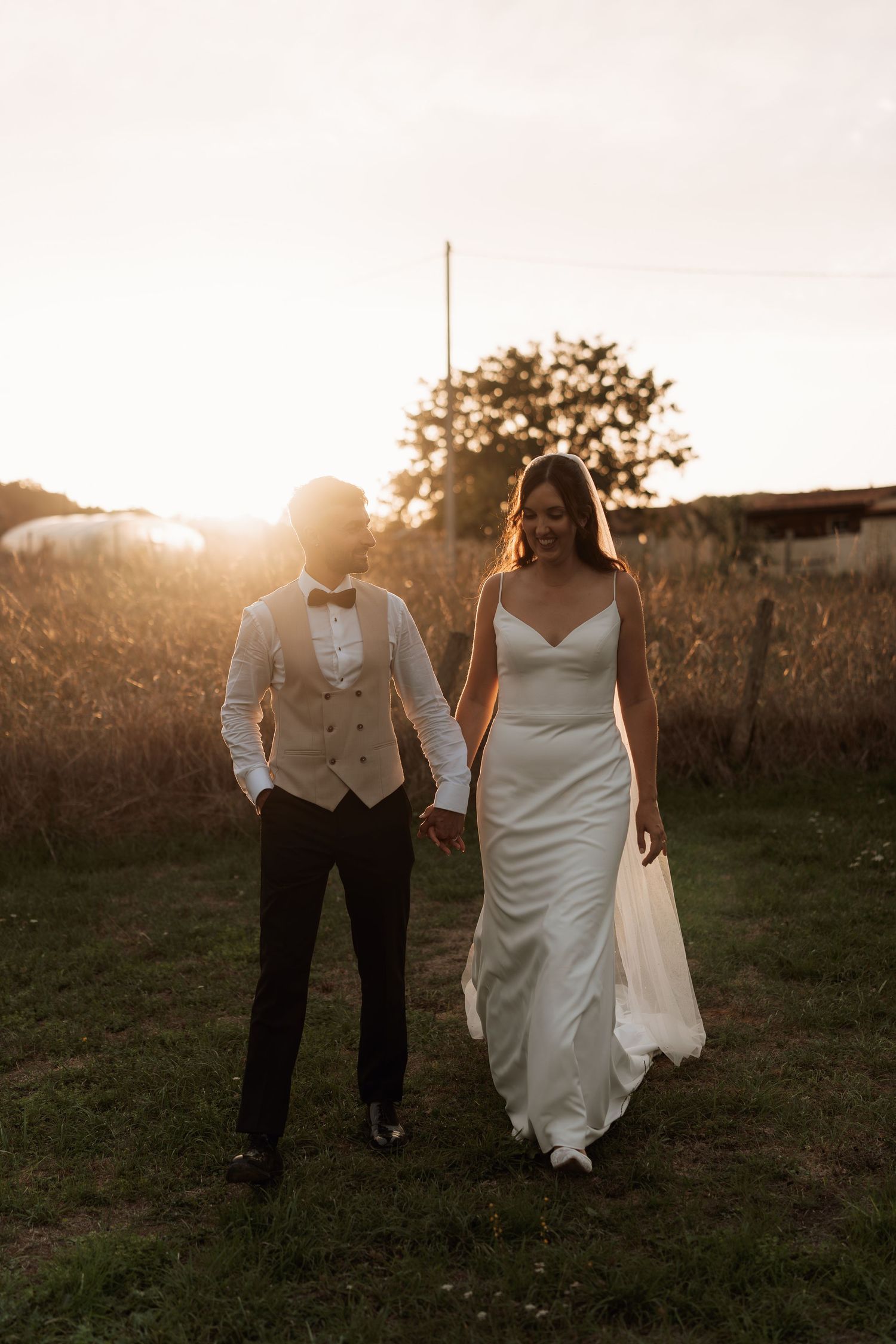 A couple walks through a field at sunset after their wedding ceremony.