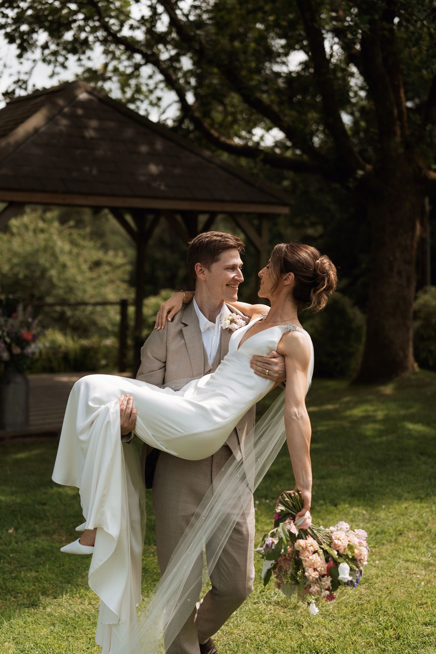A couple performs a romantic dip pose in a garden setting with flowing white dress and gray suit.