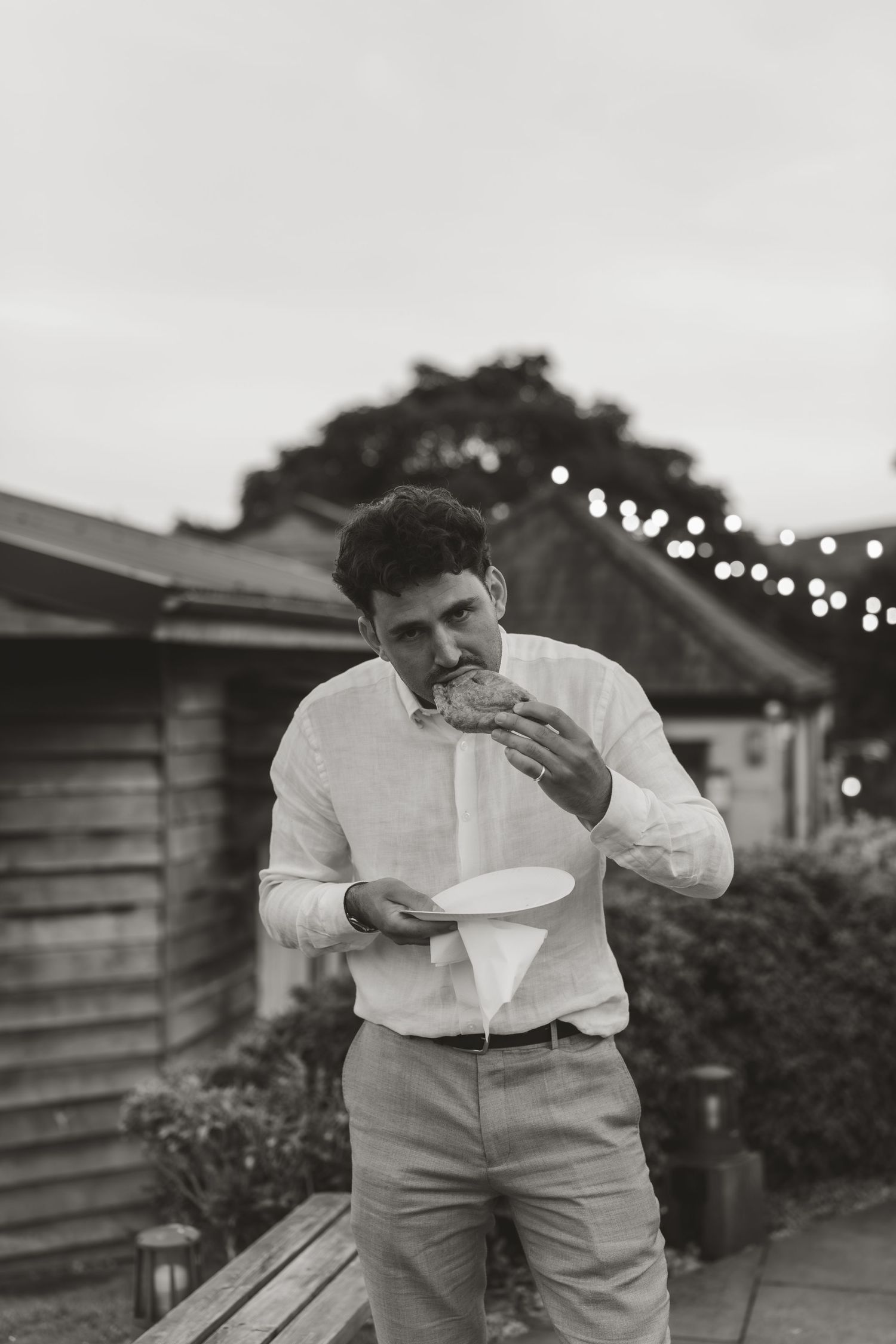 Person in formal attire eating messily at an outdoor evening reception.