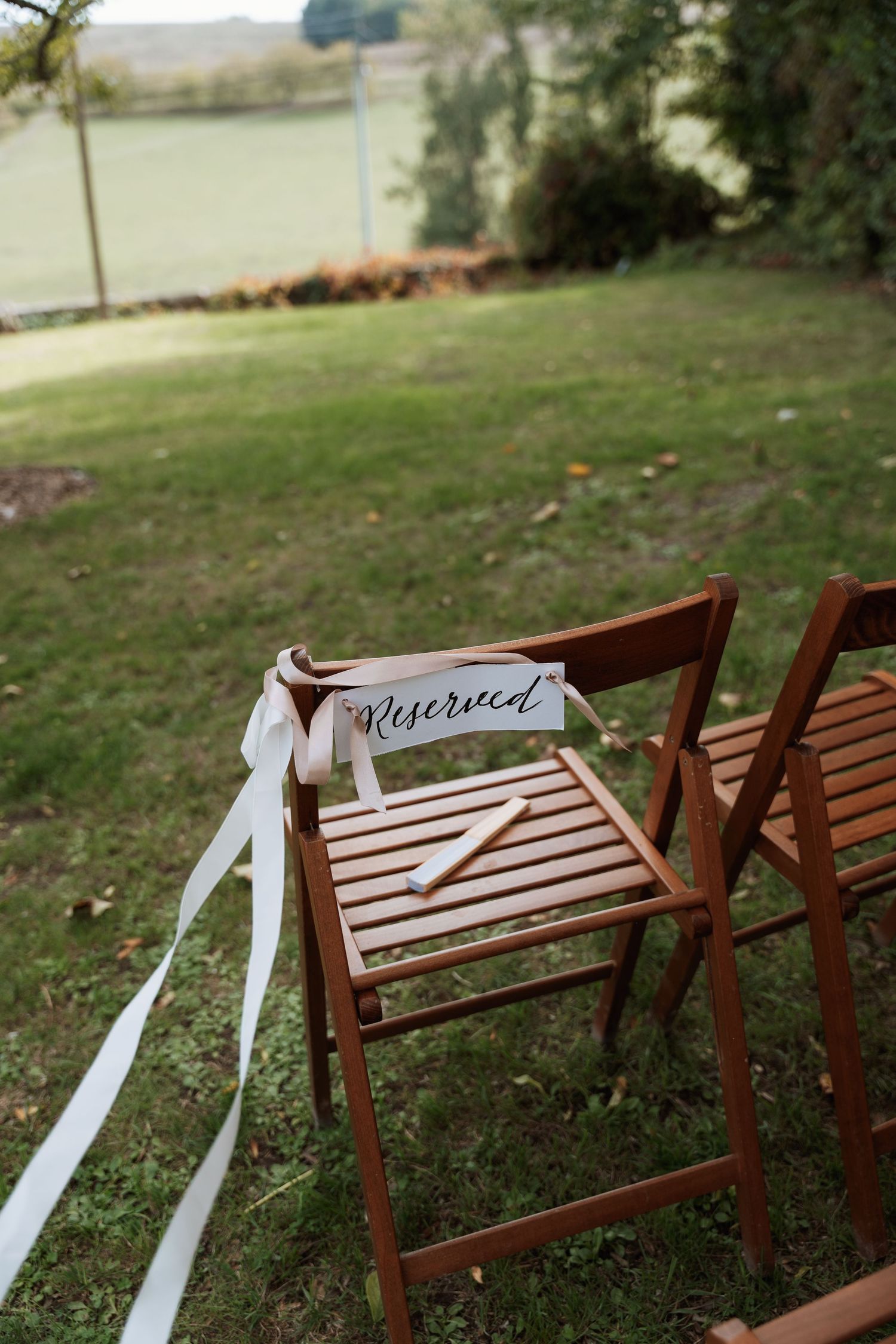 Wooden chairs with white ribbons and a 'Reserved' sign arranged for an outdoor wedding ceremony.
