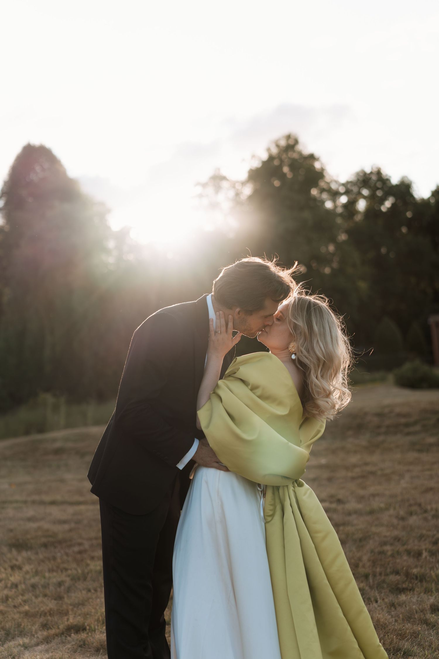 A couple embraces in a sunlit field during golden hour as their silhouettes merge against the warm evening light.