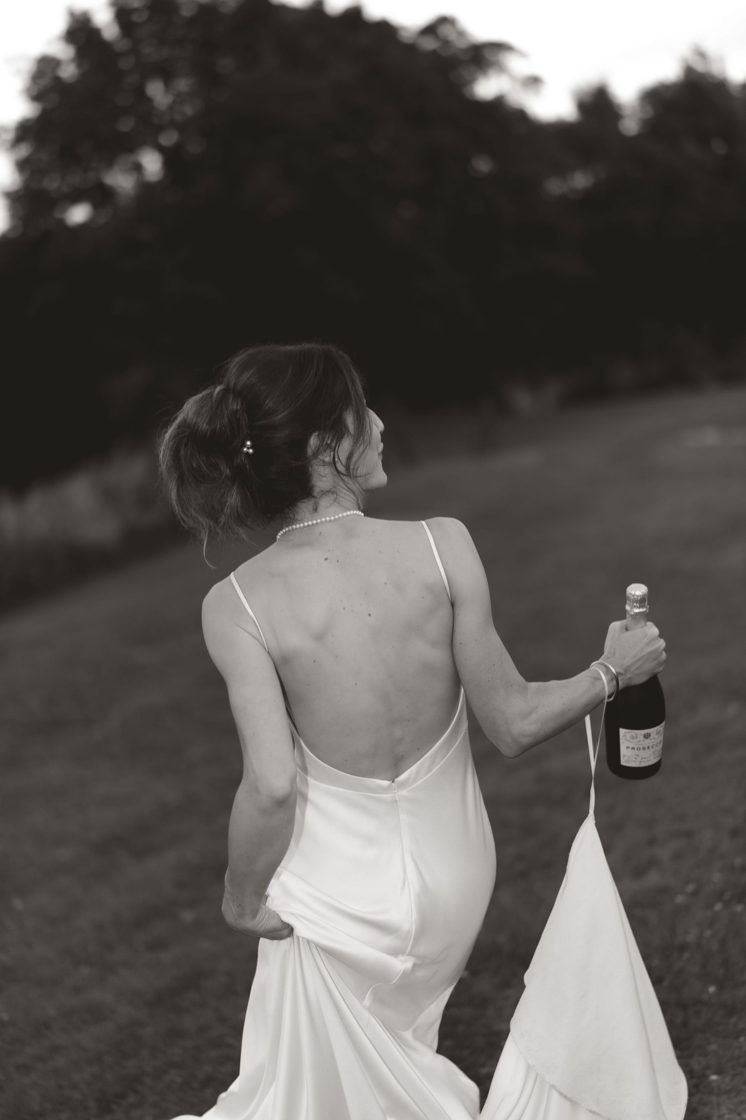 Black and white photo of someone holding a wedding dress in an outdoor setting.