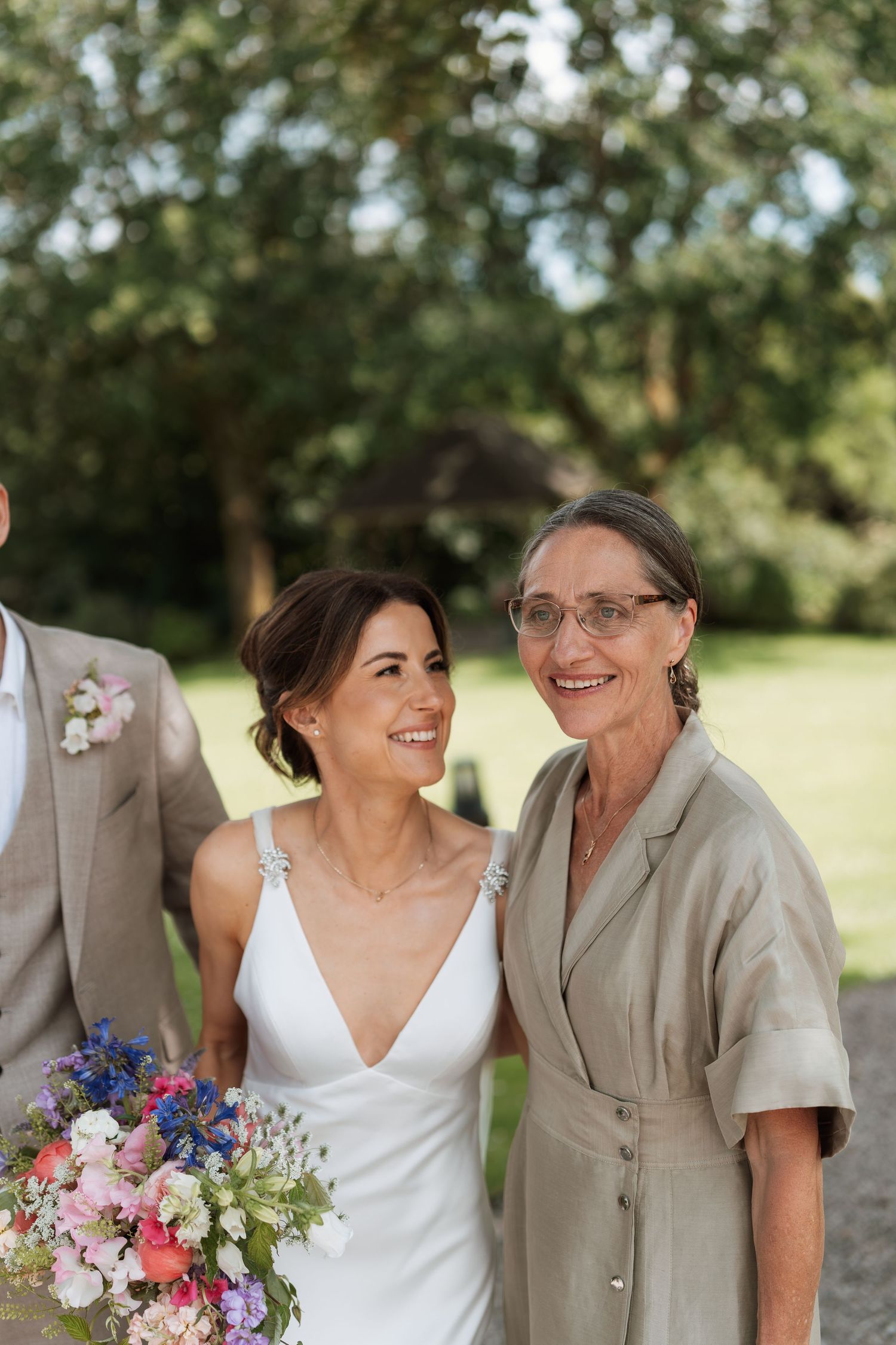 Wedding party members share joyful moments together while holding colorful bouquets outdoors.