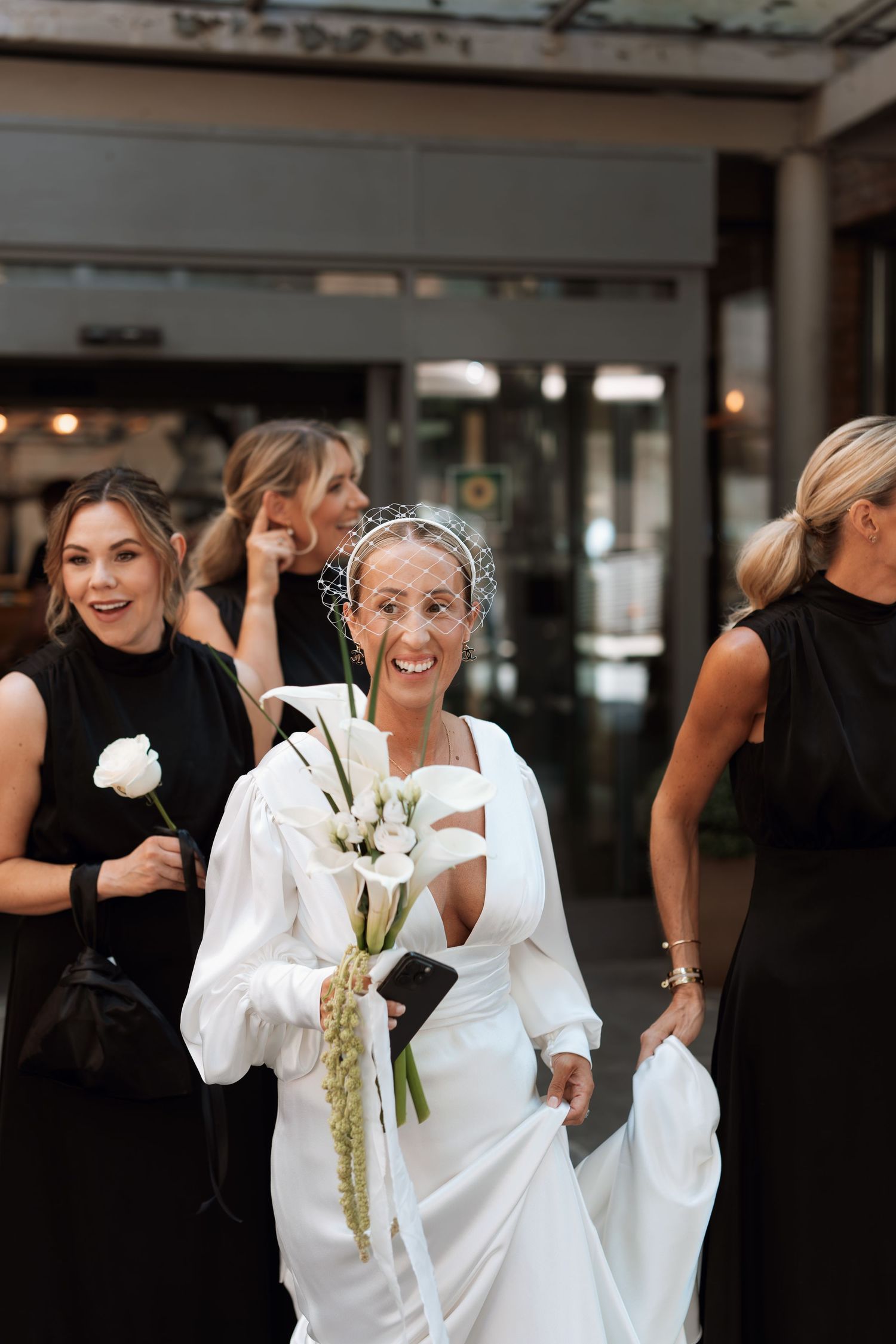 A group of women in black and white dresses gather together at an elegant event, holding white floral bouquets.
