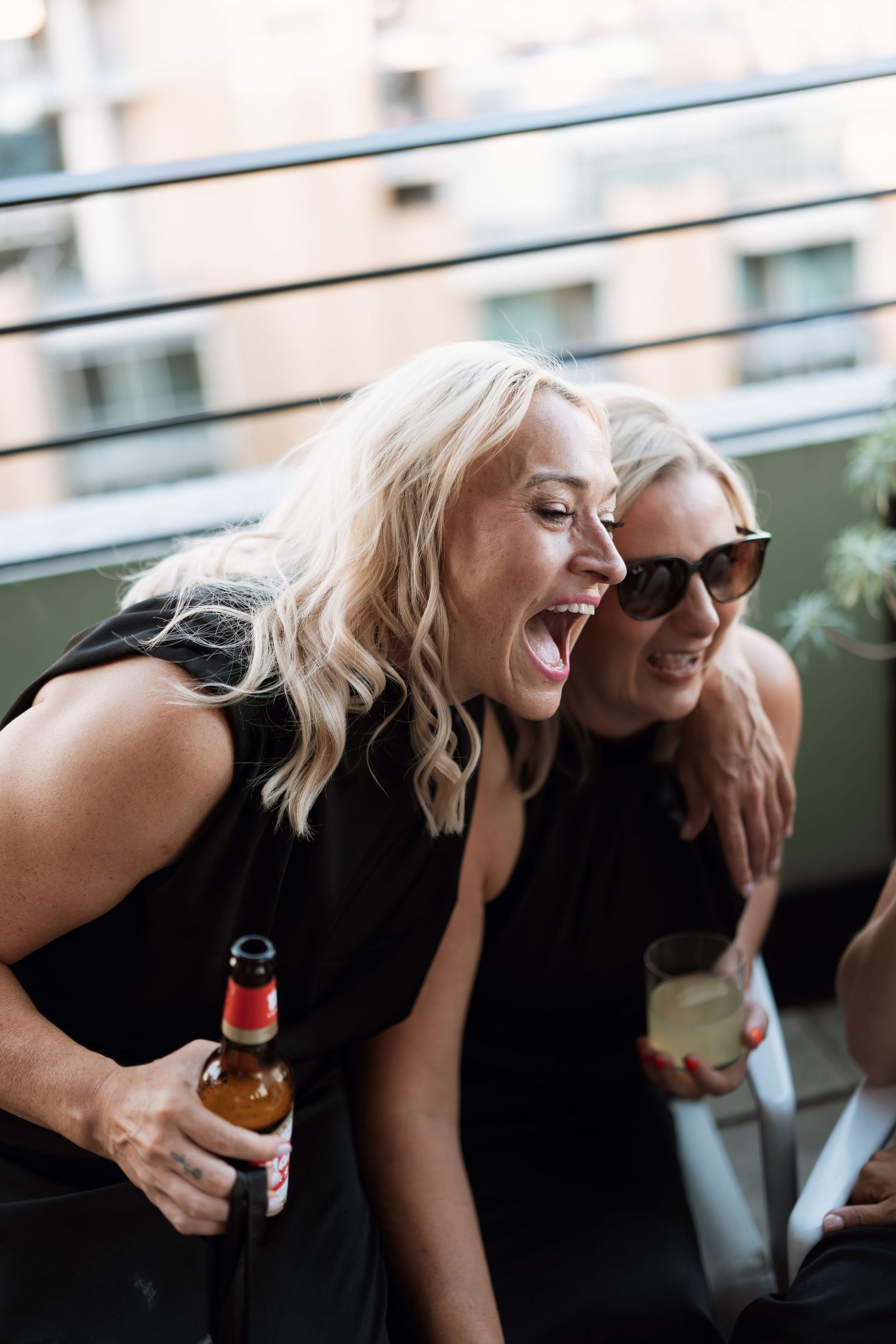 Two people laughing and enjoying drinks together on a balcony.