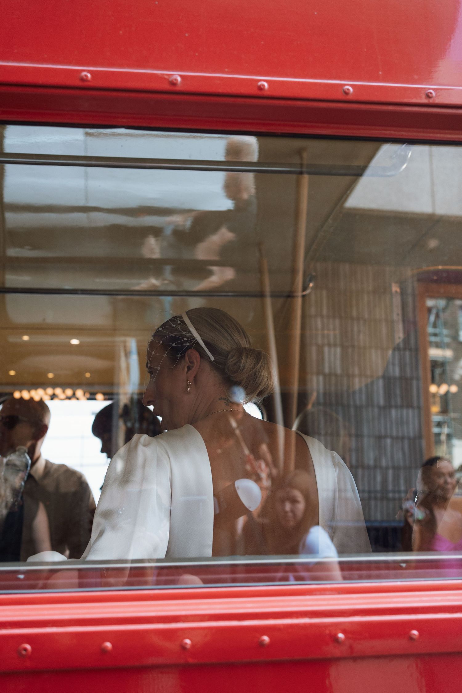 Wedding guests look out the windows of a bright red double decker bus.