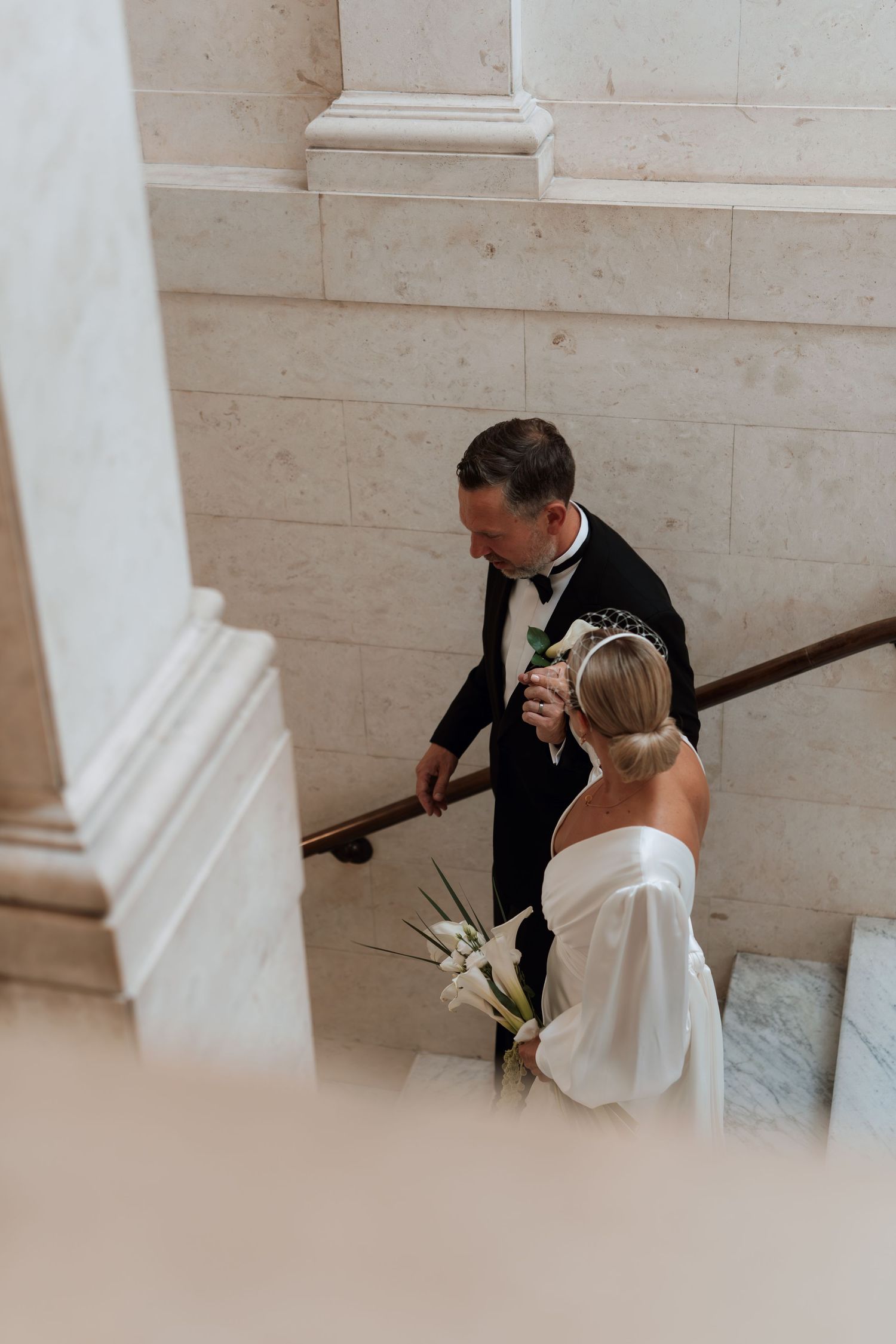 Elegant couple in wedding attire descending marble stairs.