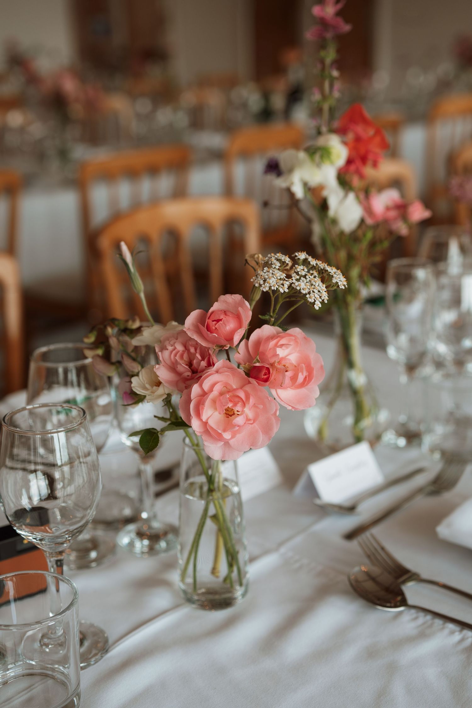 Elegant wedding table settings with pink roses in glass vases and white linens.