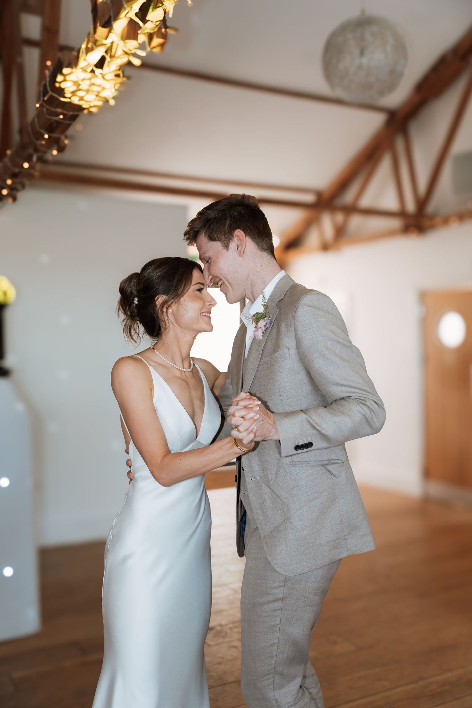 A couple shares their first dance in a rustic venue with twinkling lights overhead.
