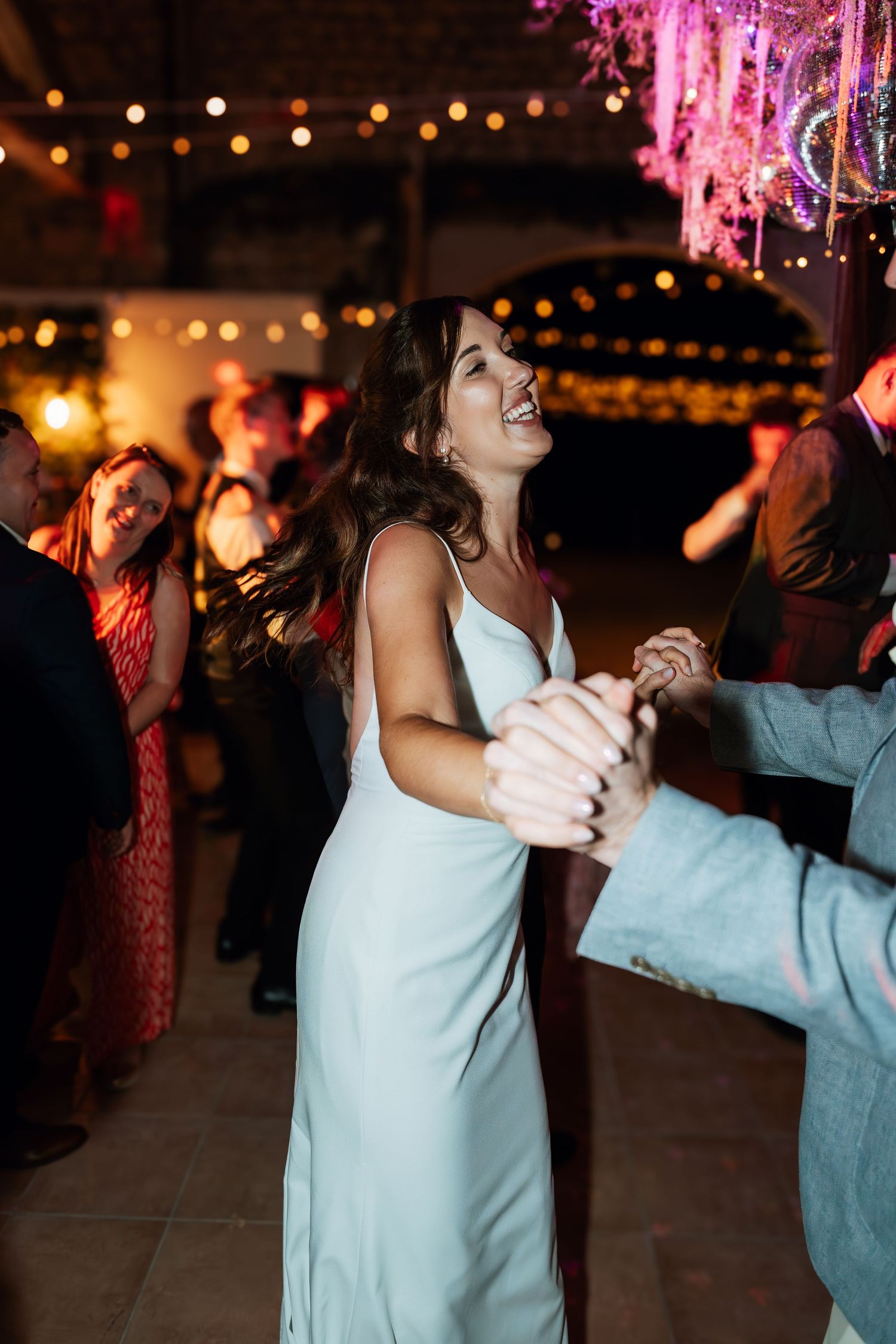 Couples dancing under string lights and pink decorations at a nighttime wedding reception.