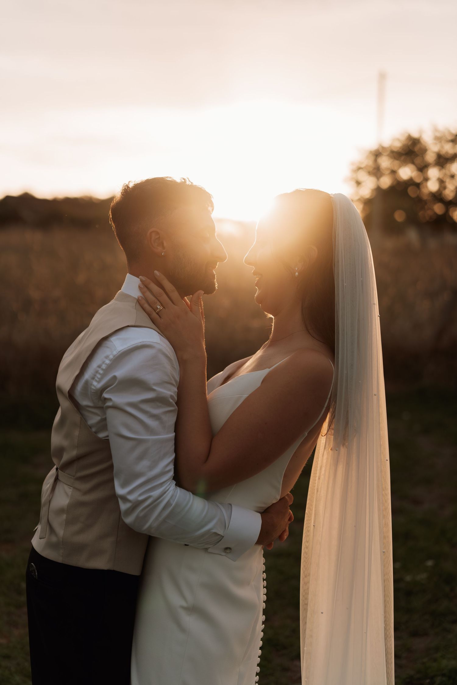 Romantic sunset wedding portrait with flowing veil and golden light.