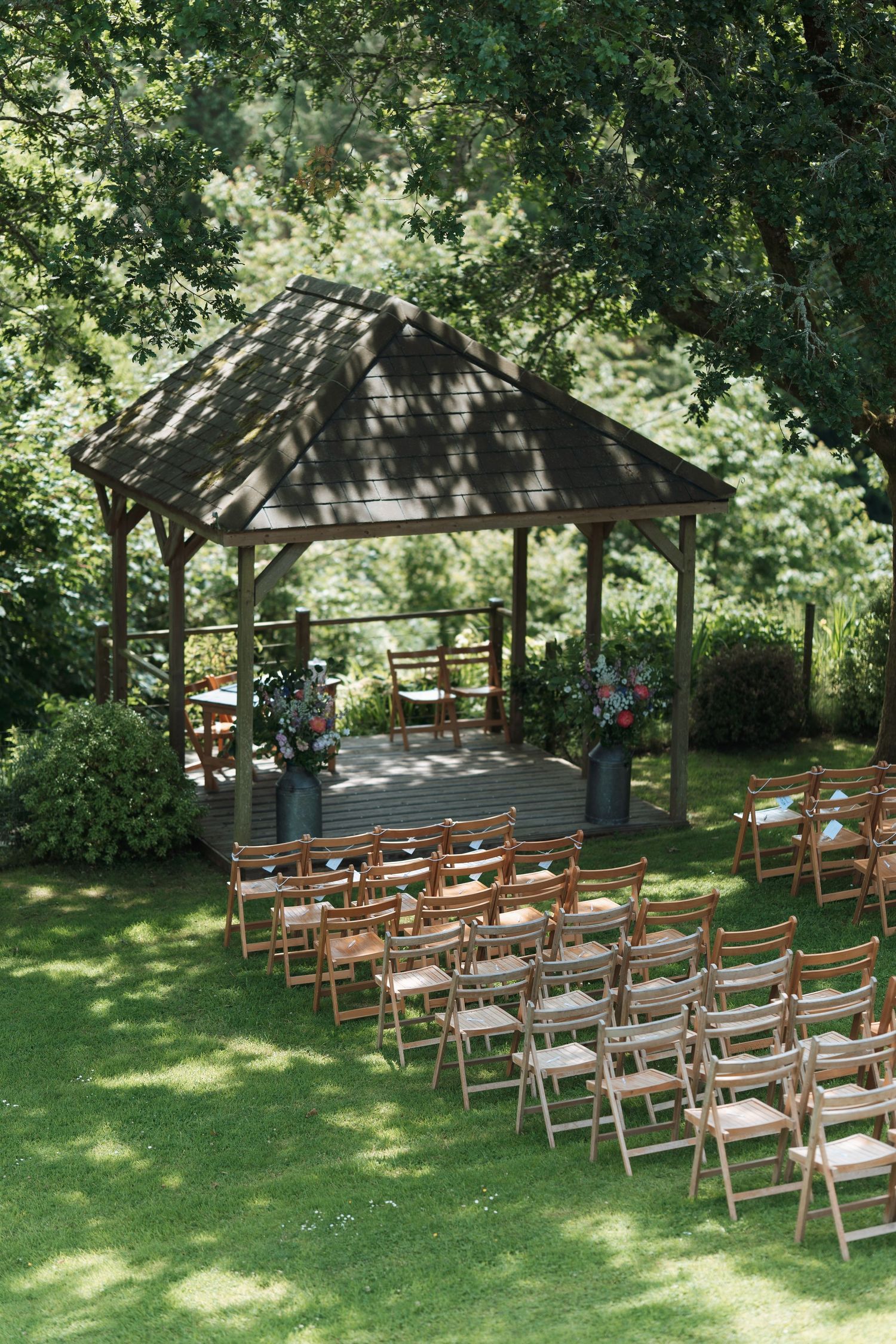 Wooden chairs arranged in rows for an outdoor wedding ceremony under a rustic gazebo.