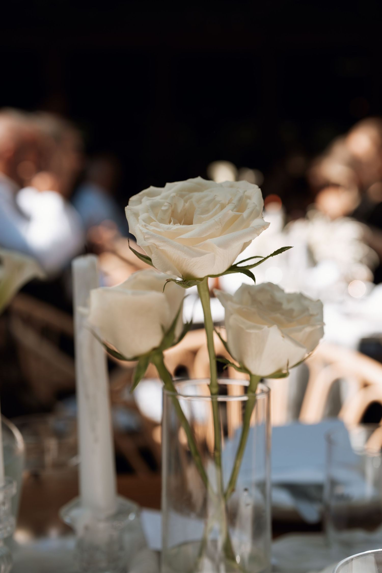 White roses in clear glass vases arranged on elegant reception tables.