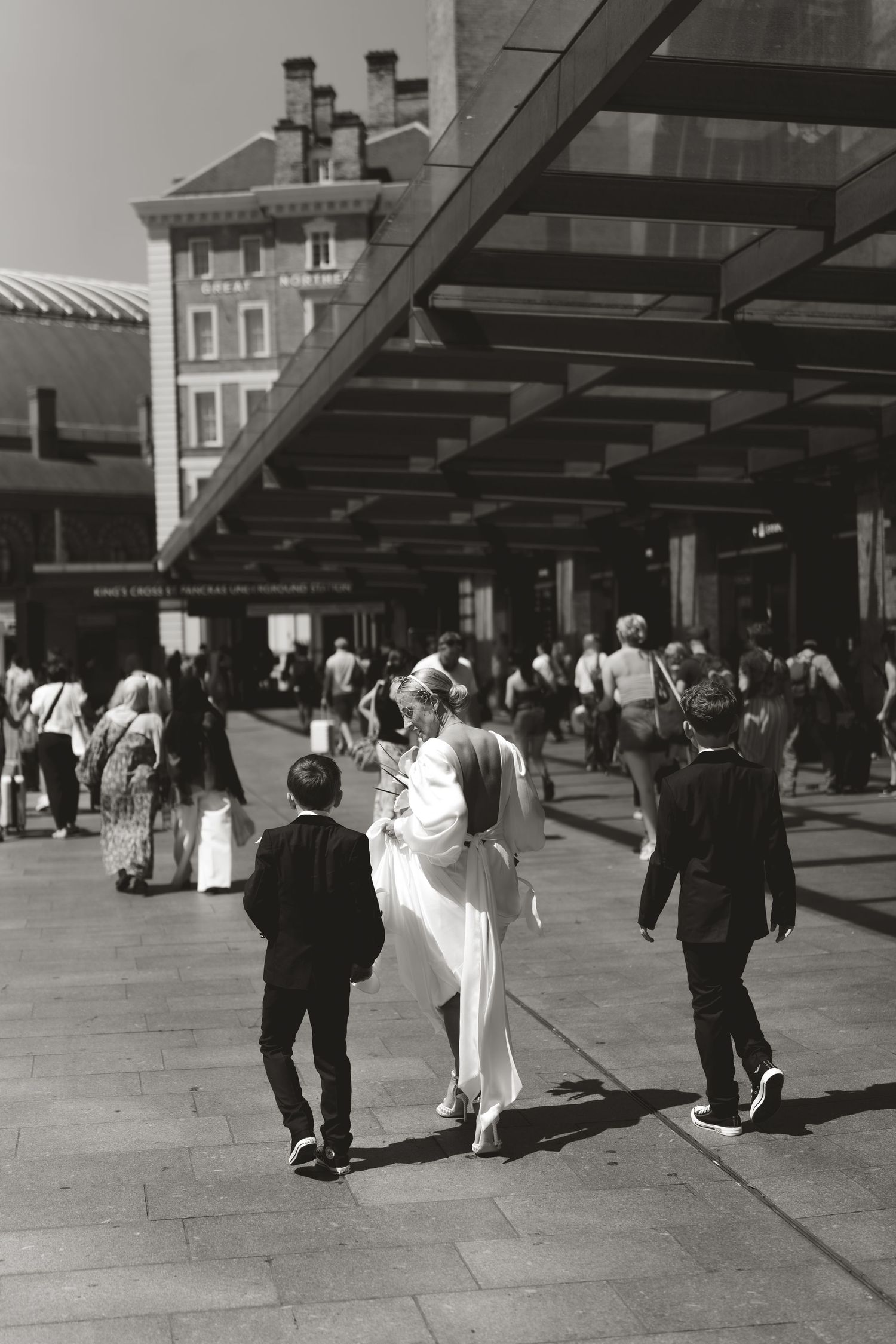 Black and white photo of people walking under a covered walkway outside a brick building.