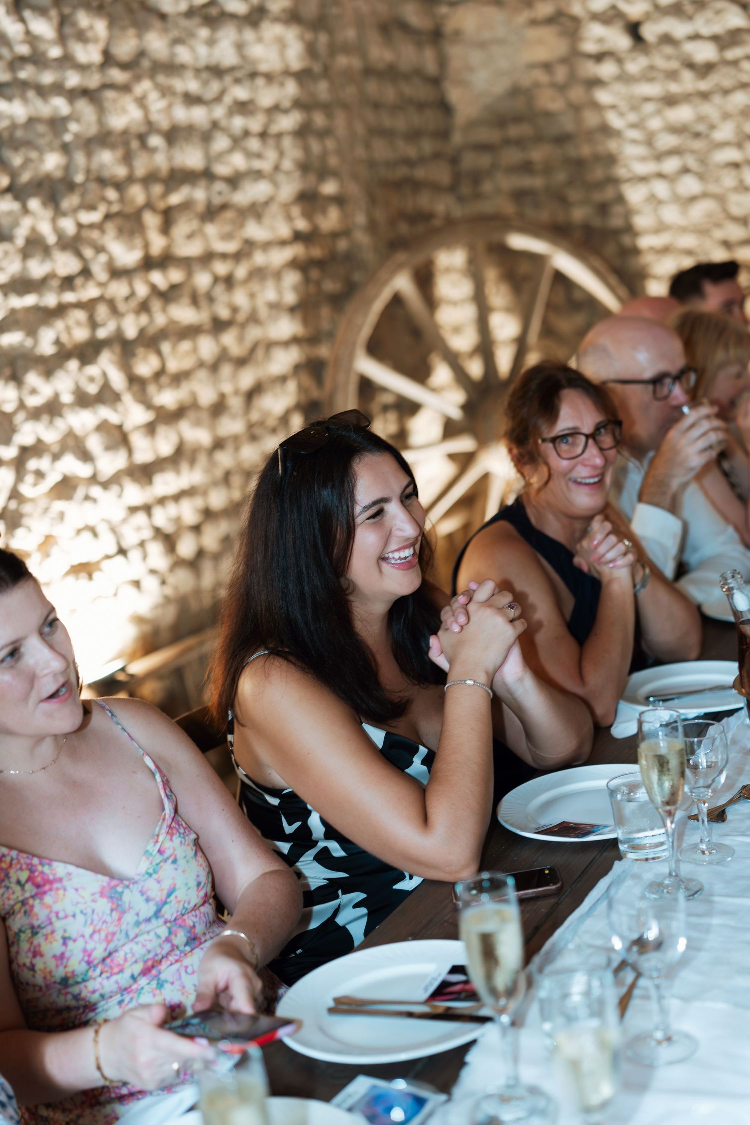 Wedding guests enjoying a meal and conversation at tables in a rustic stone venue.