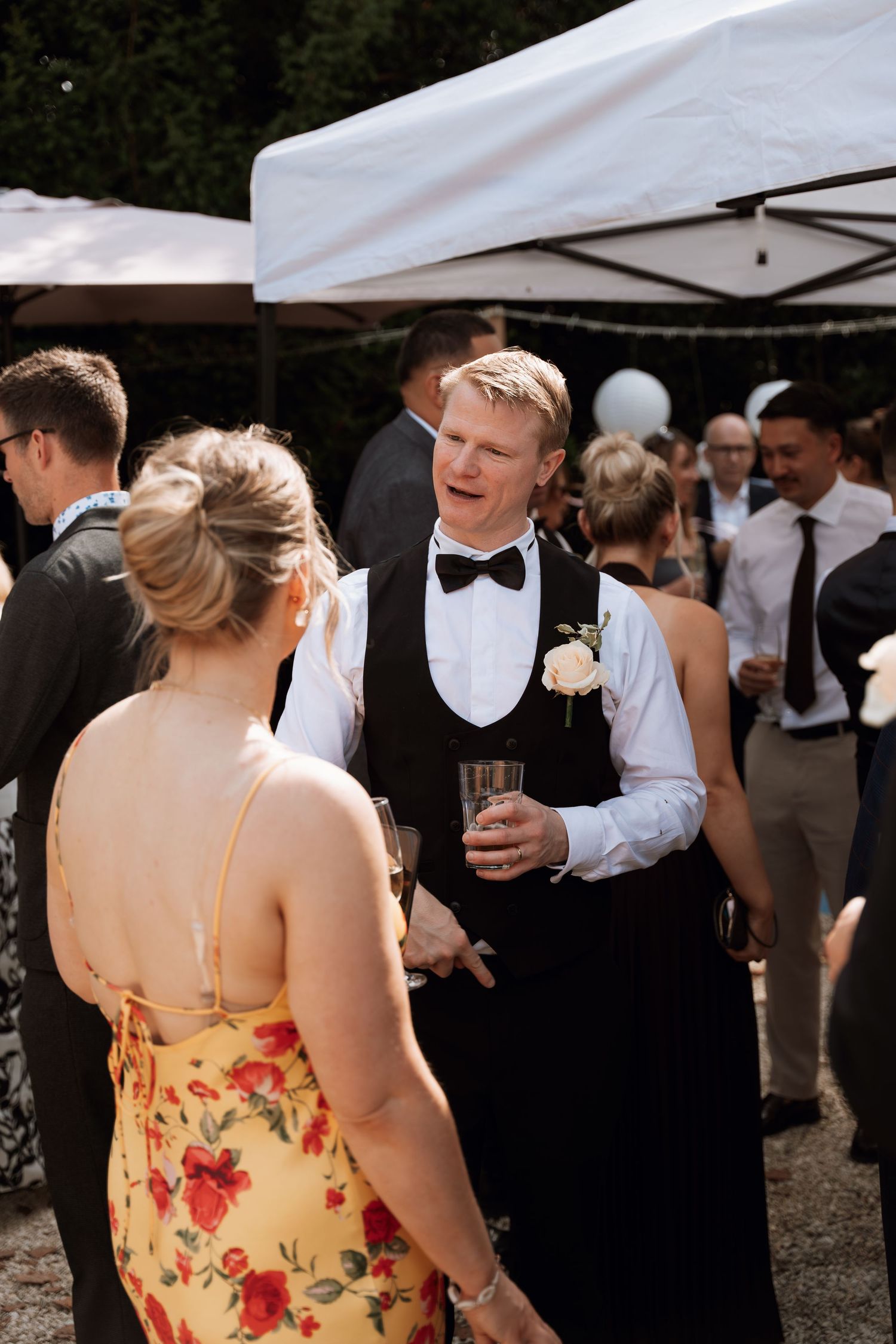 Wedding guests mingle and socialize under white outdoor tents during an elegant outdoor reception celebration.