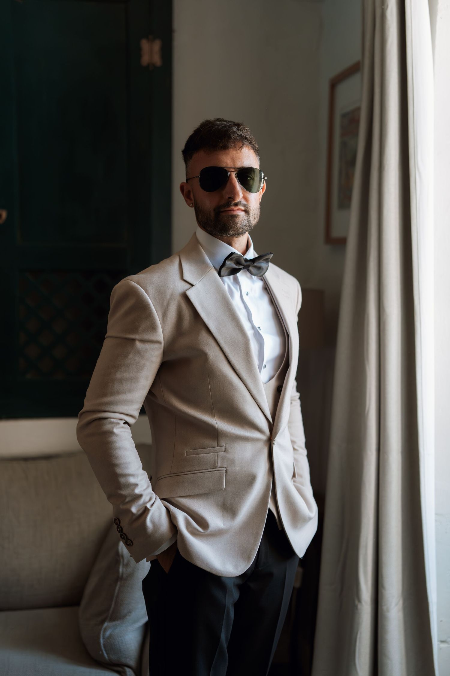 Person wearing a crisp white tuxedo jacket and bow tie posing near a window.