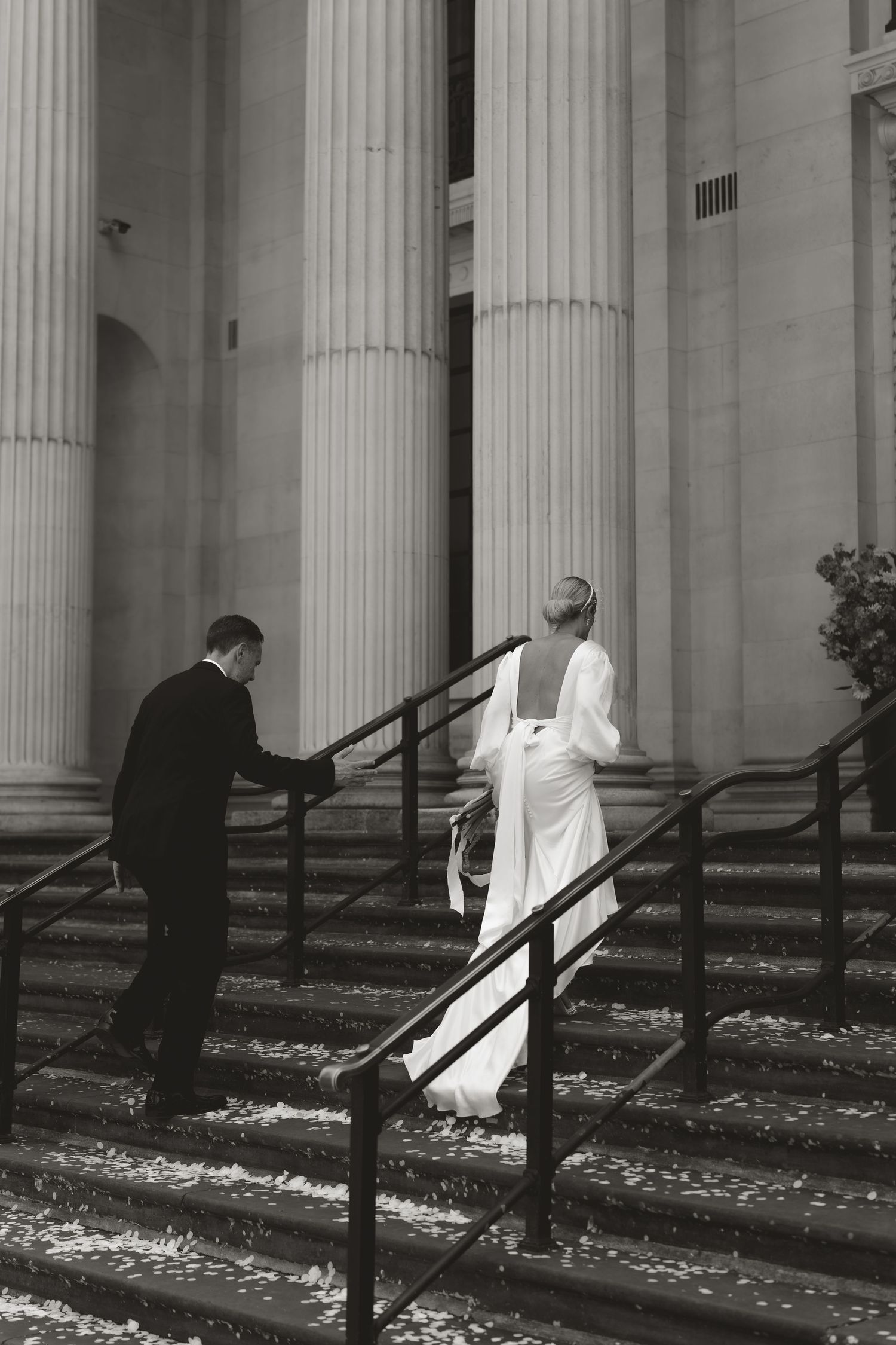 Black and white image of a columned building entrance with scattered petals on the ground.