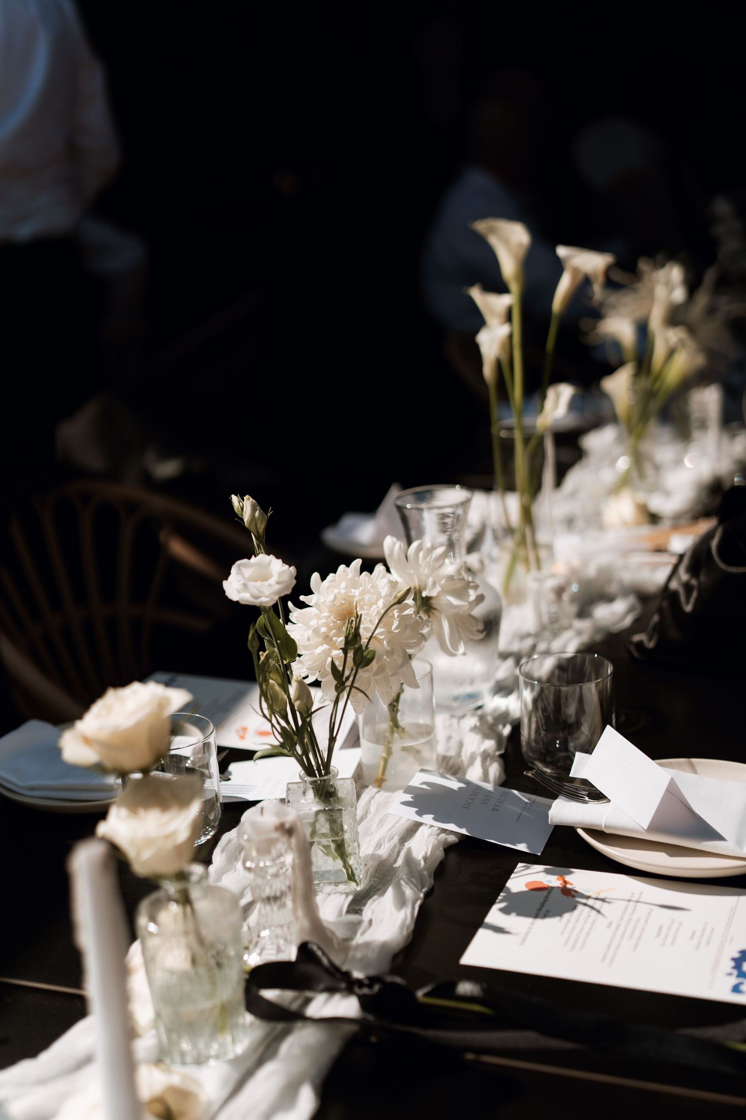 Elegant white floral table settings with calla lilies and roses arranged in glass vases at a formal dining event.