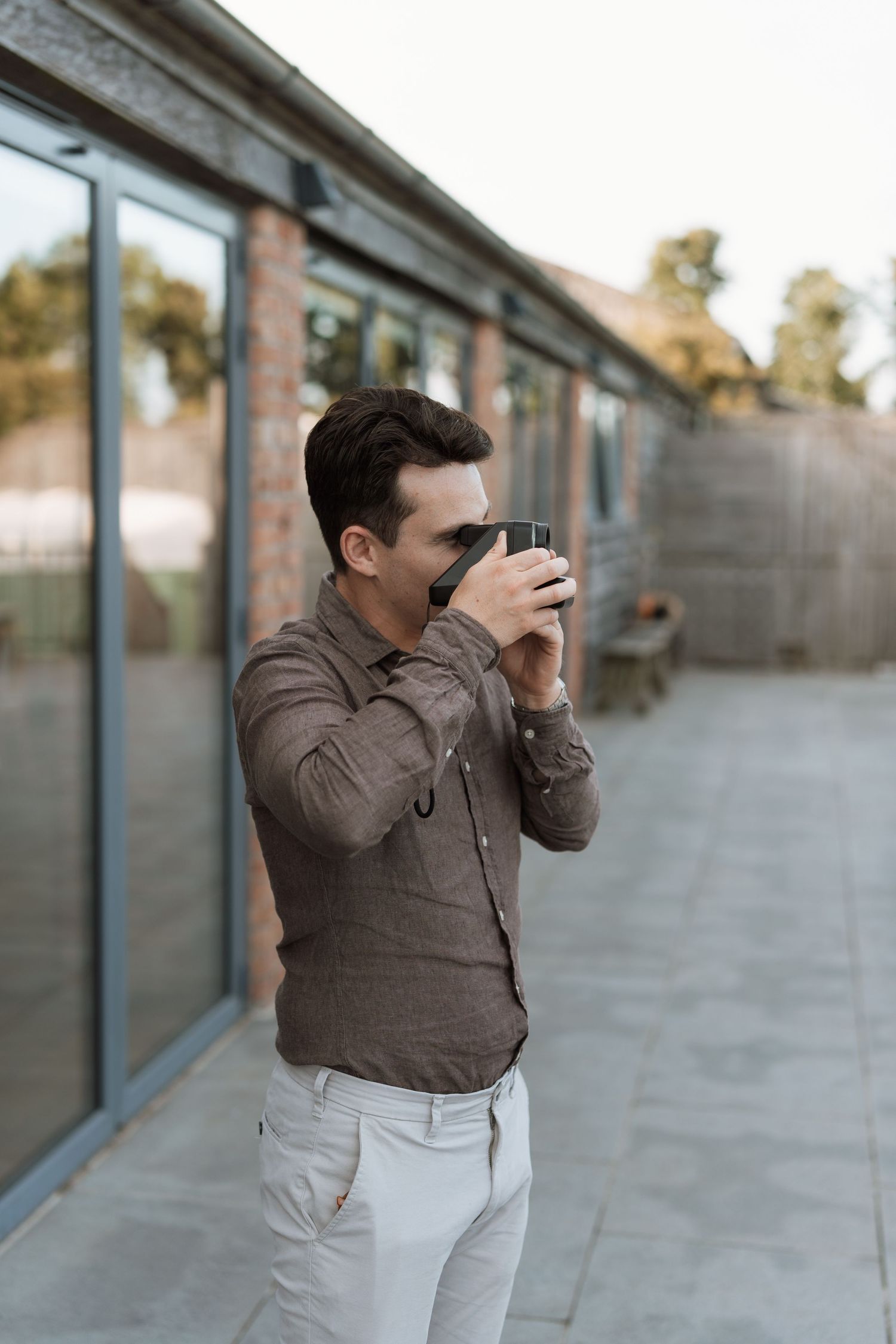 Person in brown jacket taking photos against industrial building backdrop.