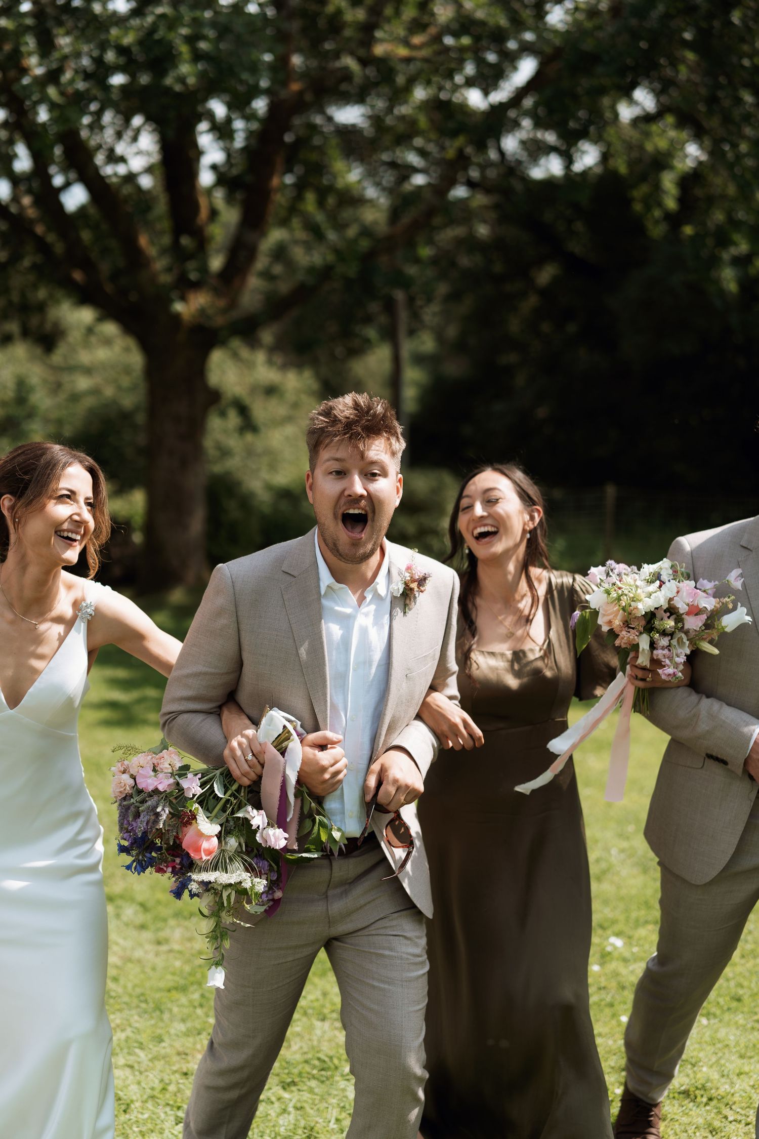 Wedding party laughing and celebrating together outdoors with bouquets.