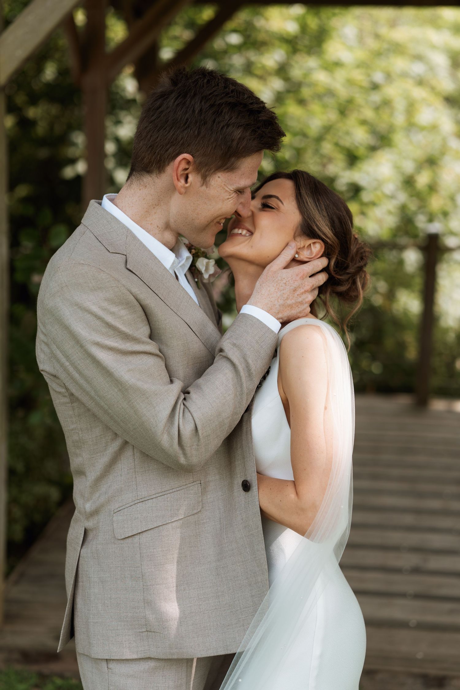 Romantic moment between newlyweds sharing a tender kiss under trees at their outdoor wedding.