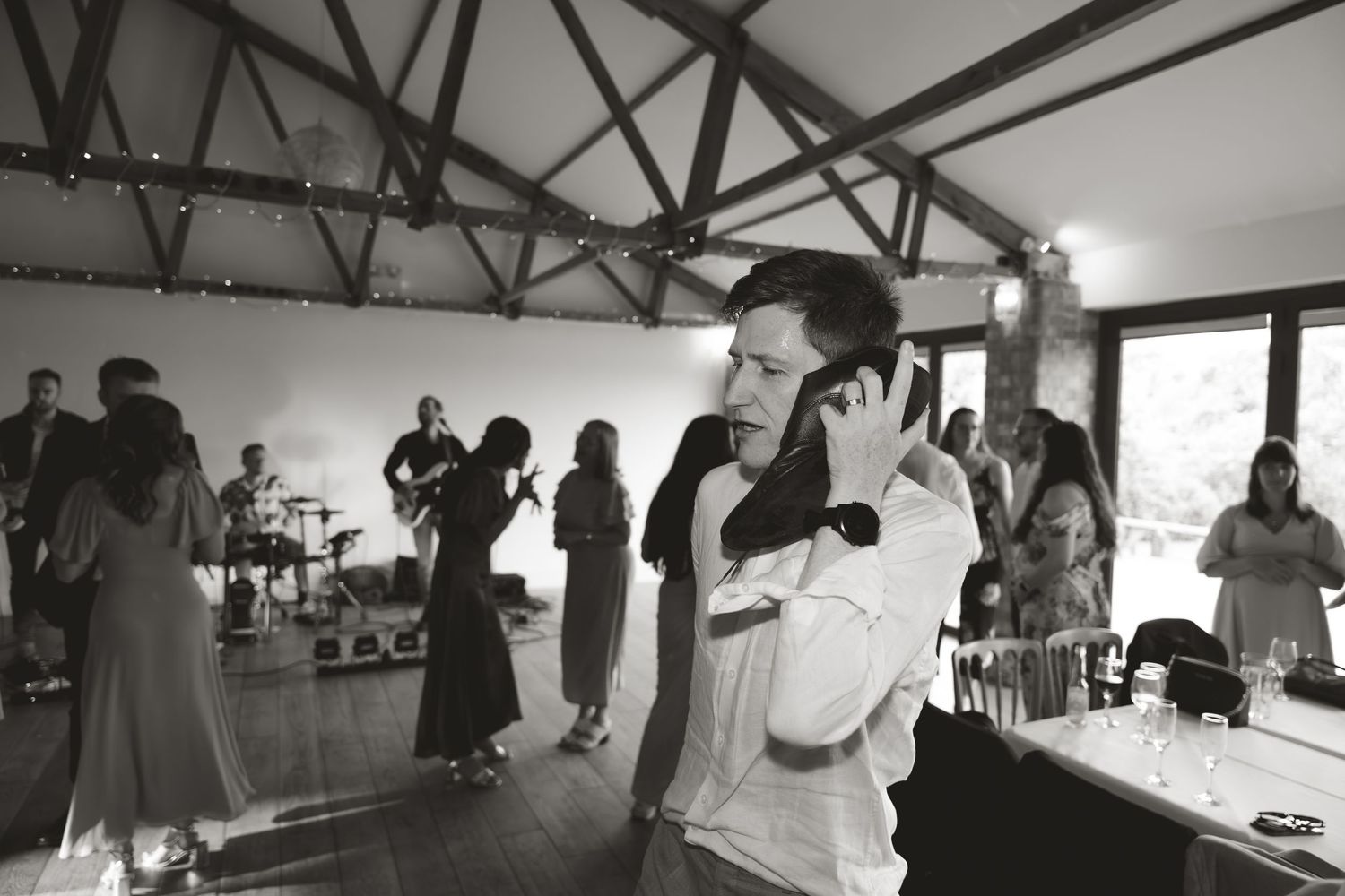 Black and white panoramic shot of wedding reception with guests dancing indoors.