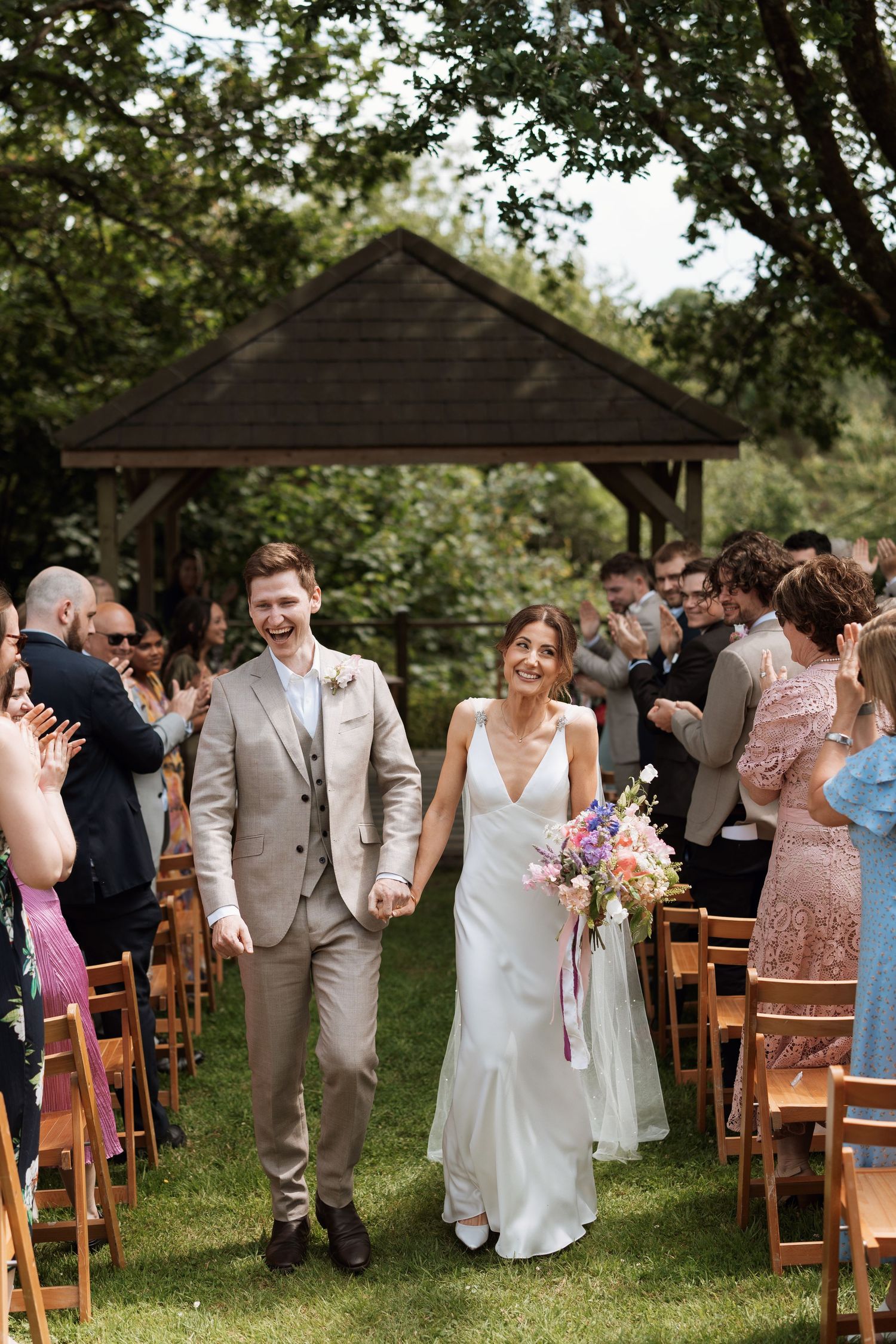 Wedding guests celebrating on wooden chairs during an outdoor garden ceremony.