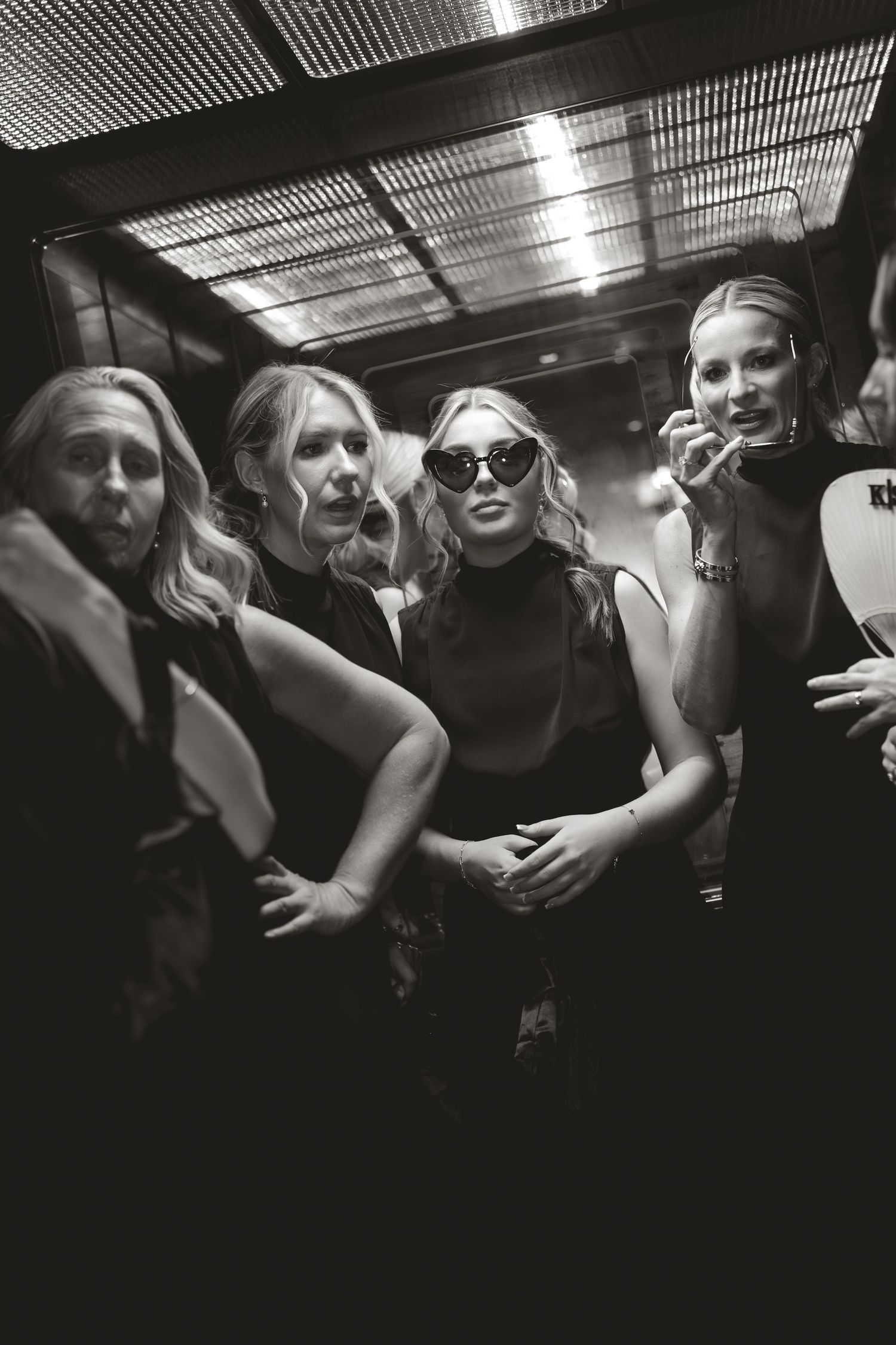 A black and white party photo shows a group posing together in a dimly lit space with dramatic lighting.