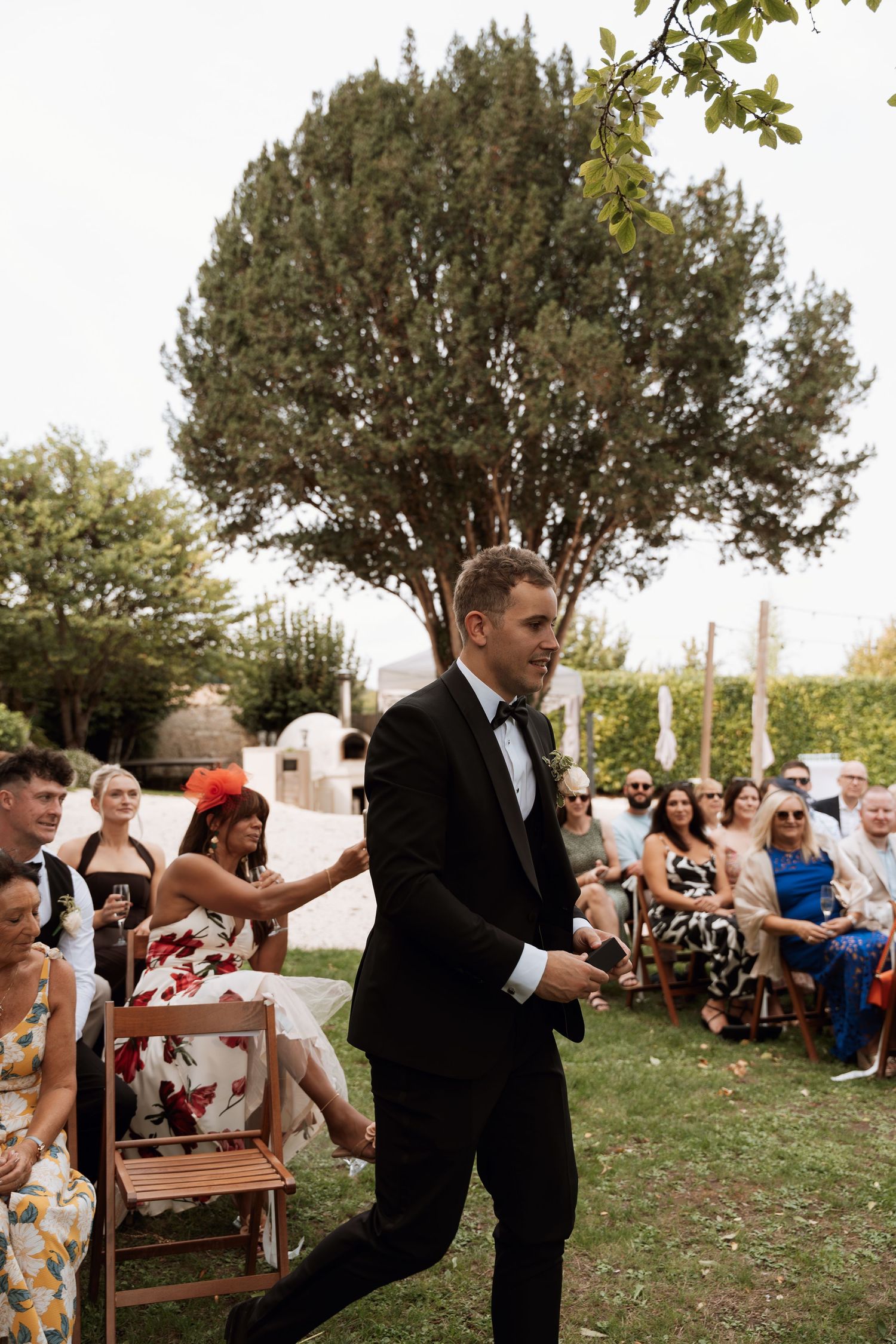 Wedding party members in formal attire perform choreographed dance moves outdoors during celebration.