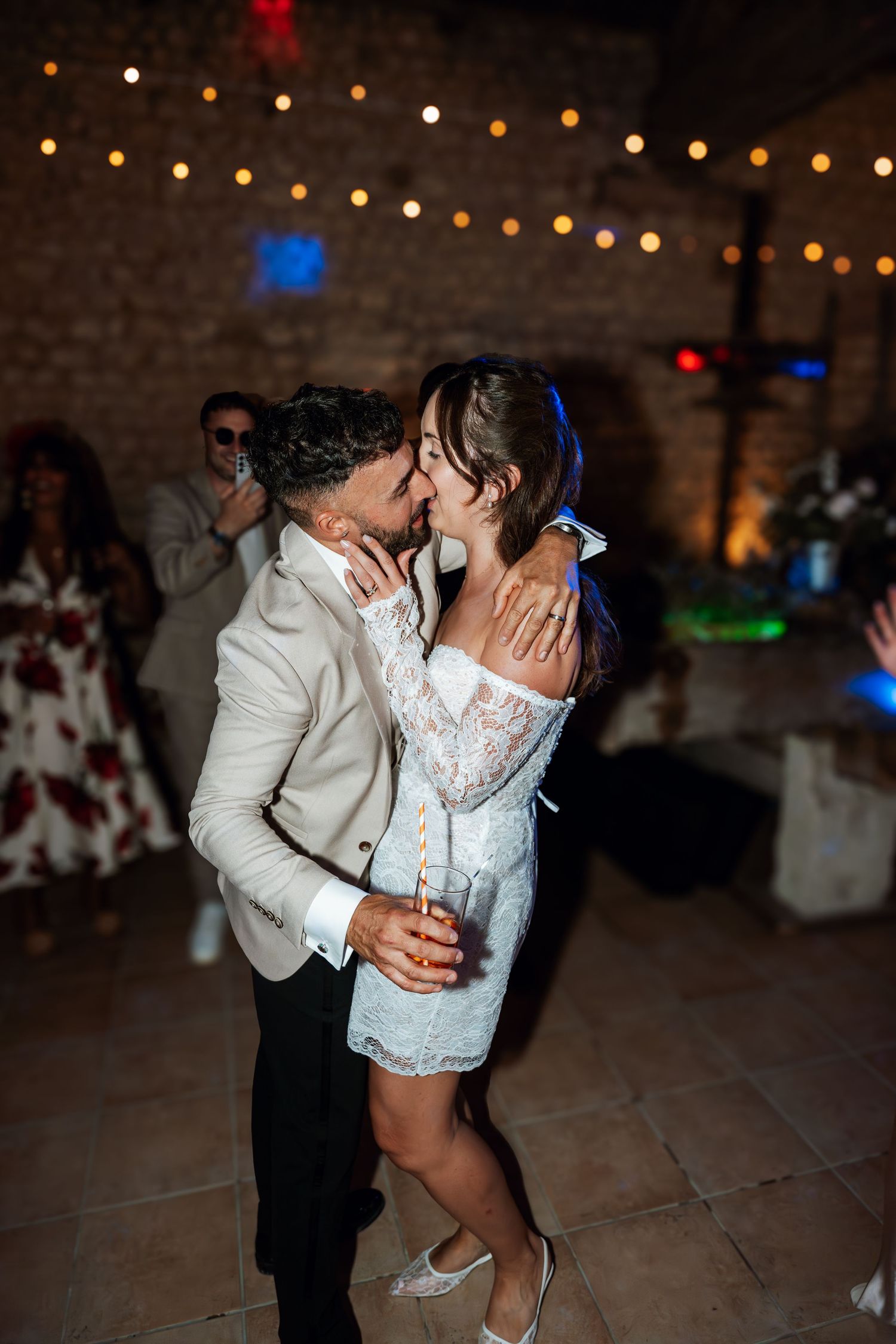 A couple shares a playful dance moment under string lights at their wedding reception.